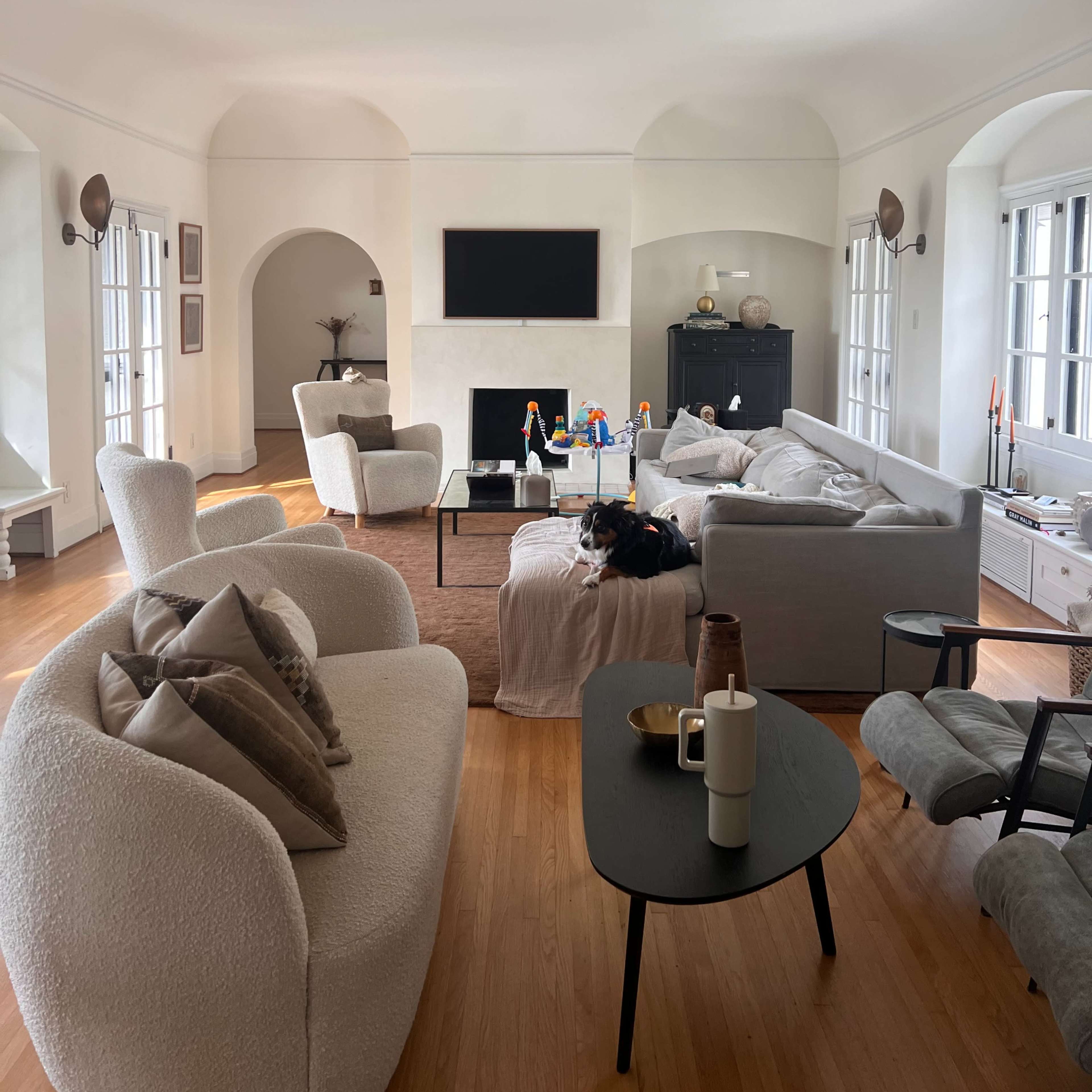 A spacious living room with light-colored furniture, a central coffee table, and a large television mounted on the wall.