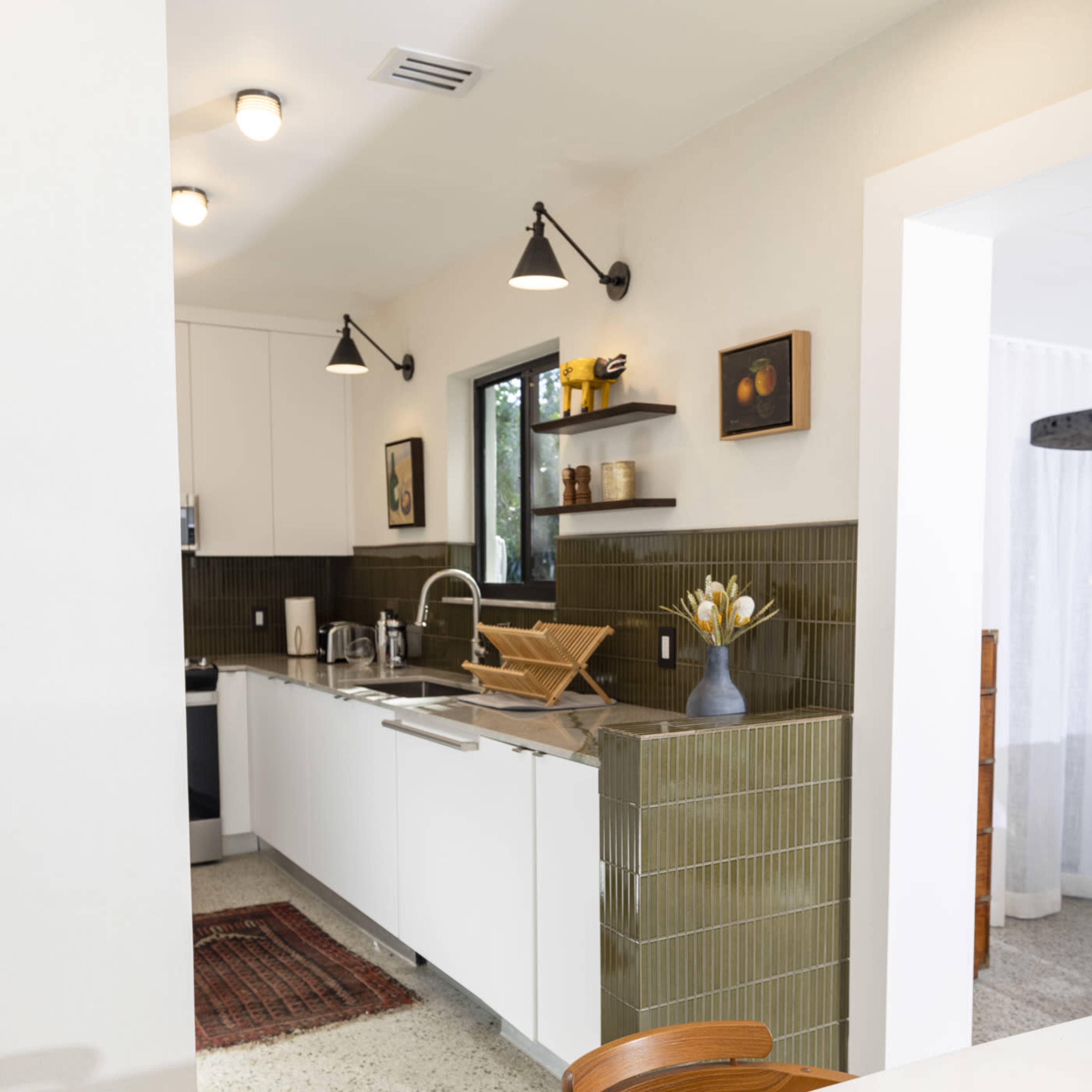 A modern kitchen with white cabinets, green tiled walls, and wooden shelves displaying decor.