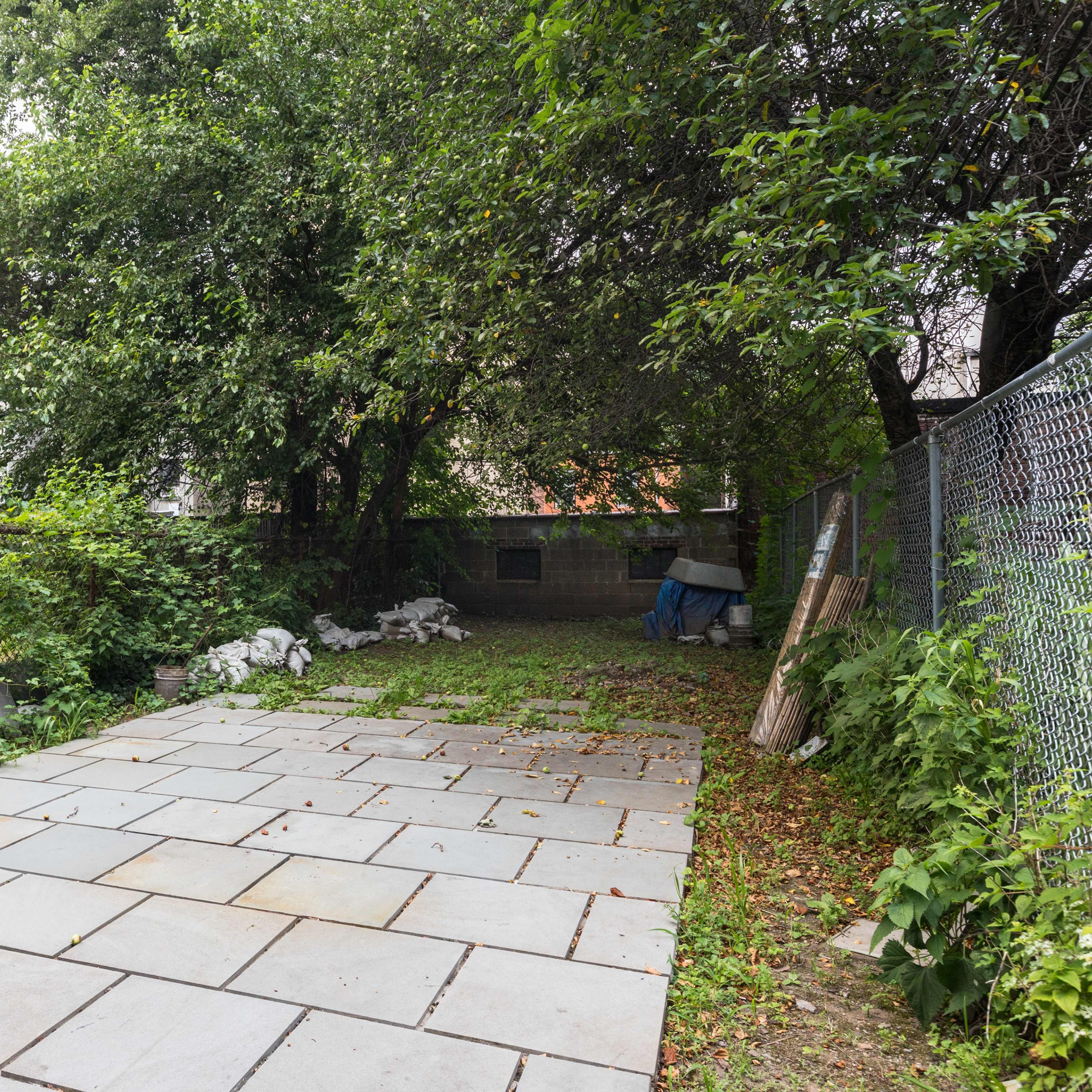 A spacious backyard with a stone patio, surrounded by greenery and a fence.