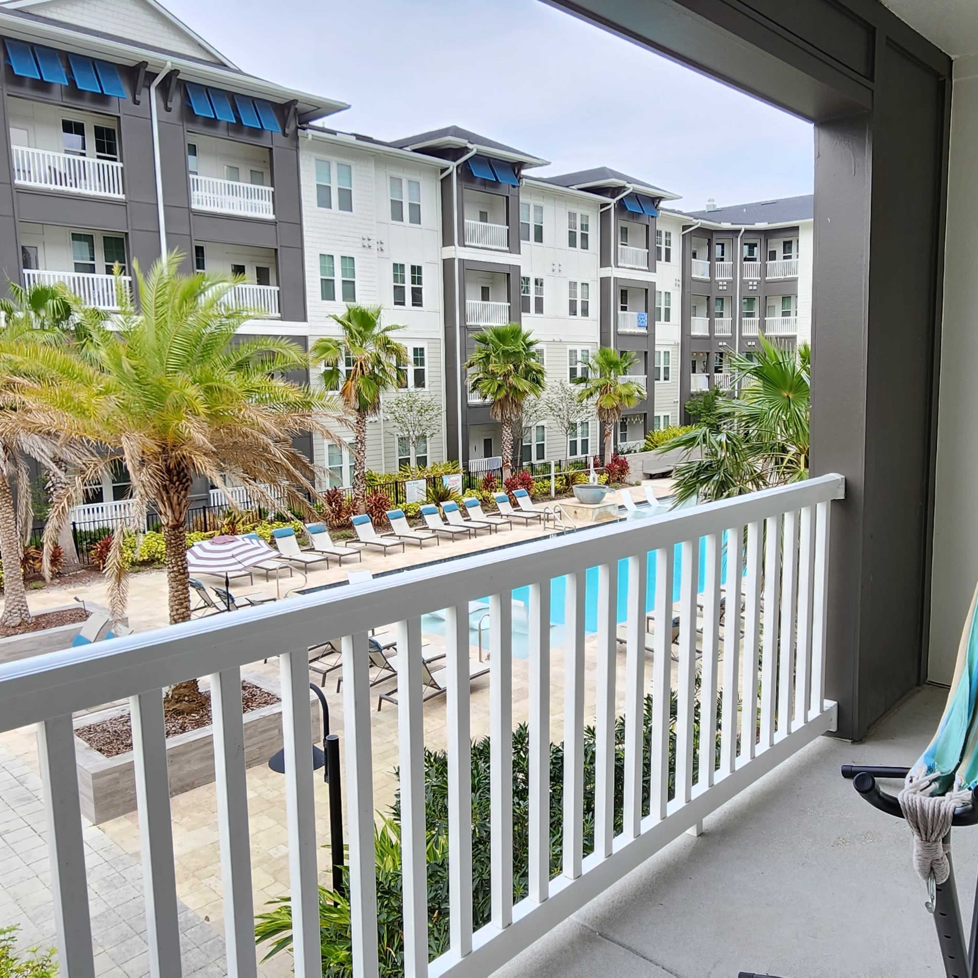 A balcony view overlooking a pool area surrounded by palm trees and apartment buildings.