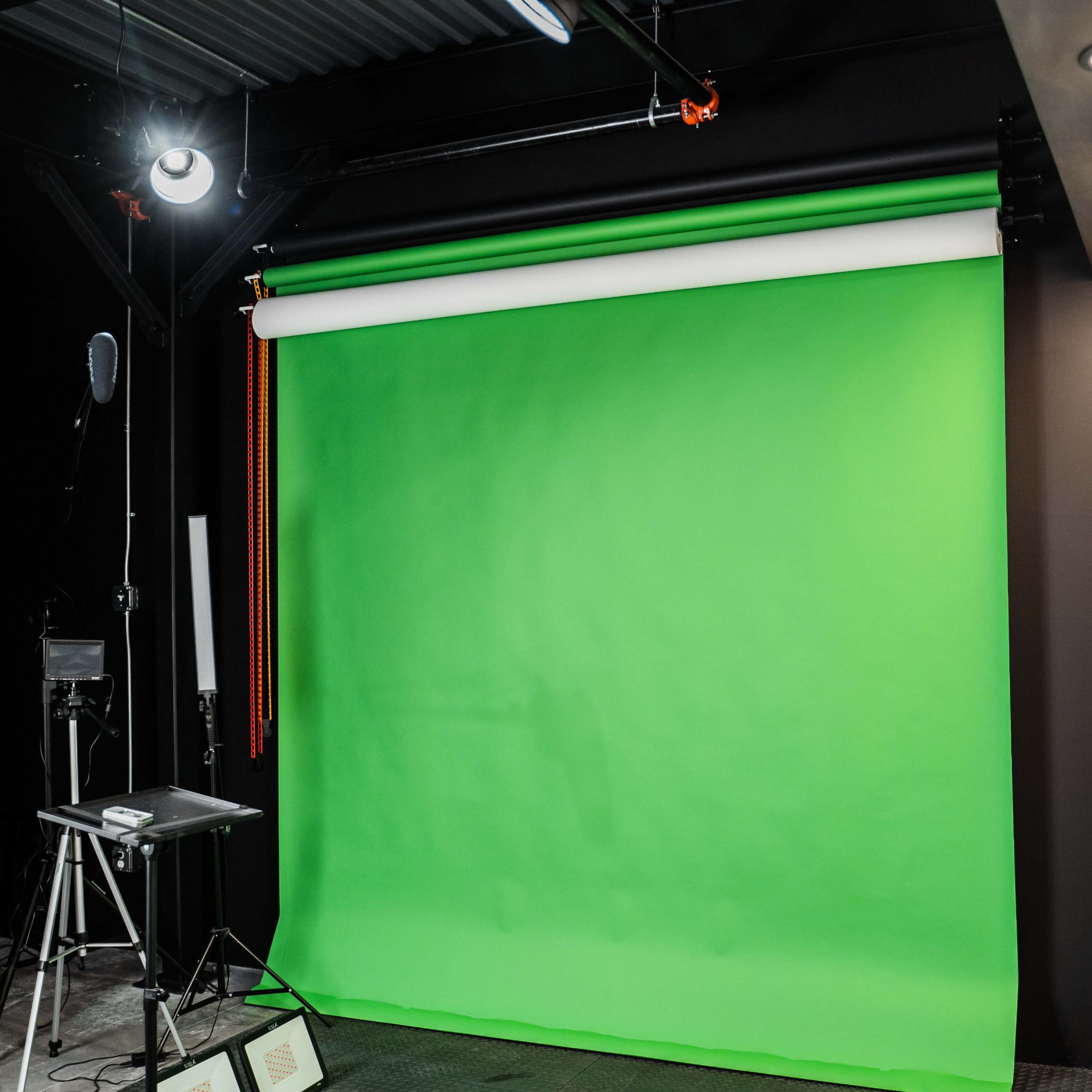 A photography studio featuring a large green backdrop and various lighting equipment.