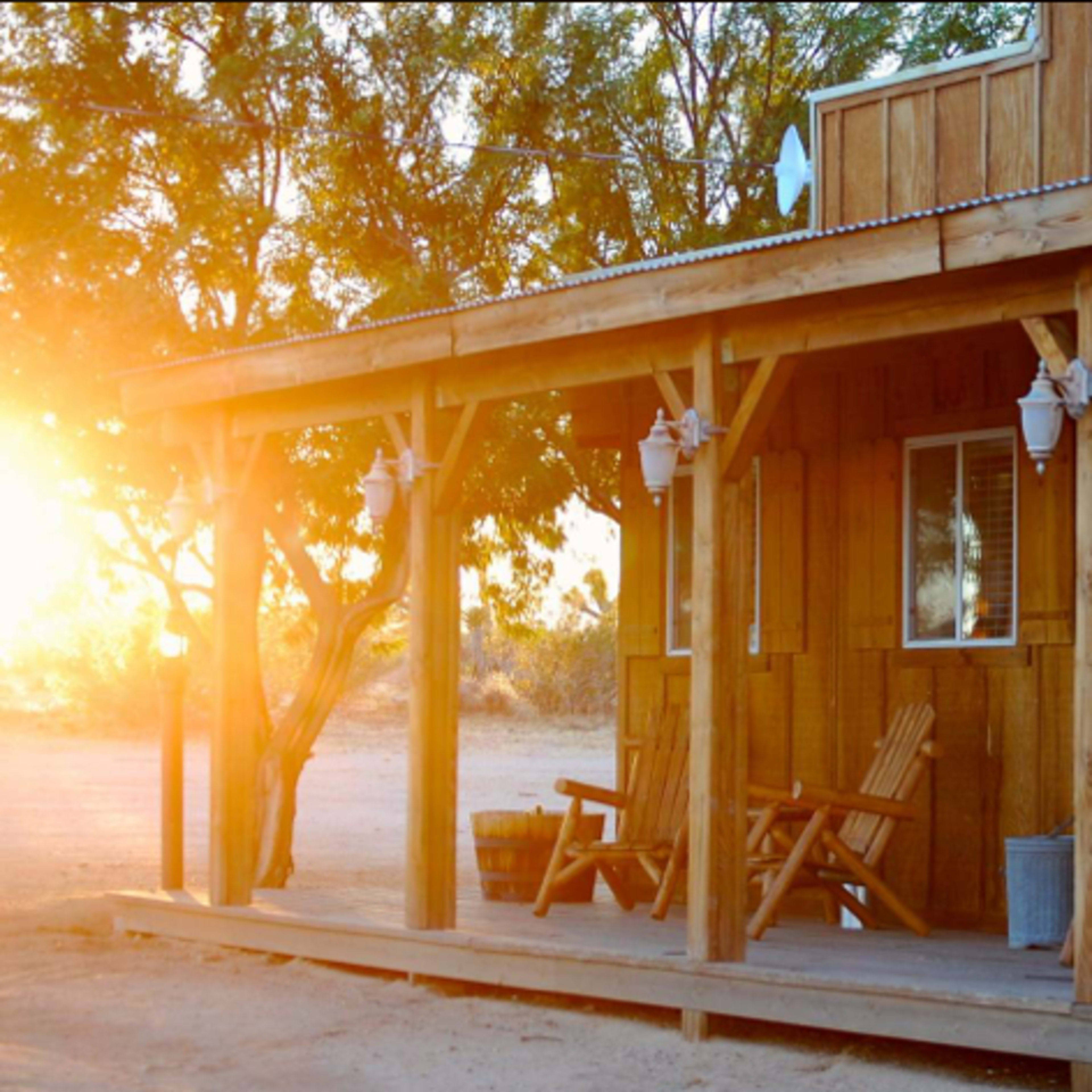 A wooden porch with several adirondack chairs and a cabin-like structure bathed in warm sunset light.