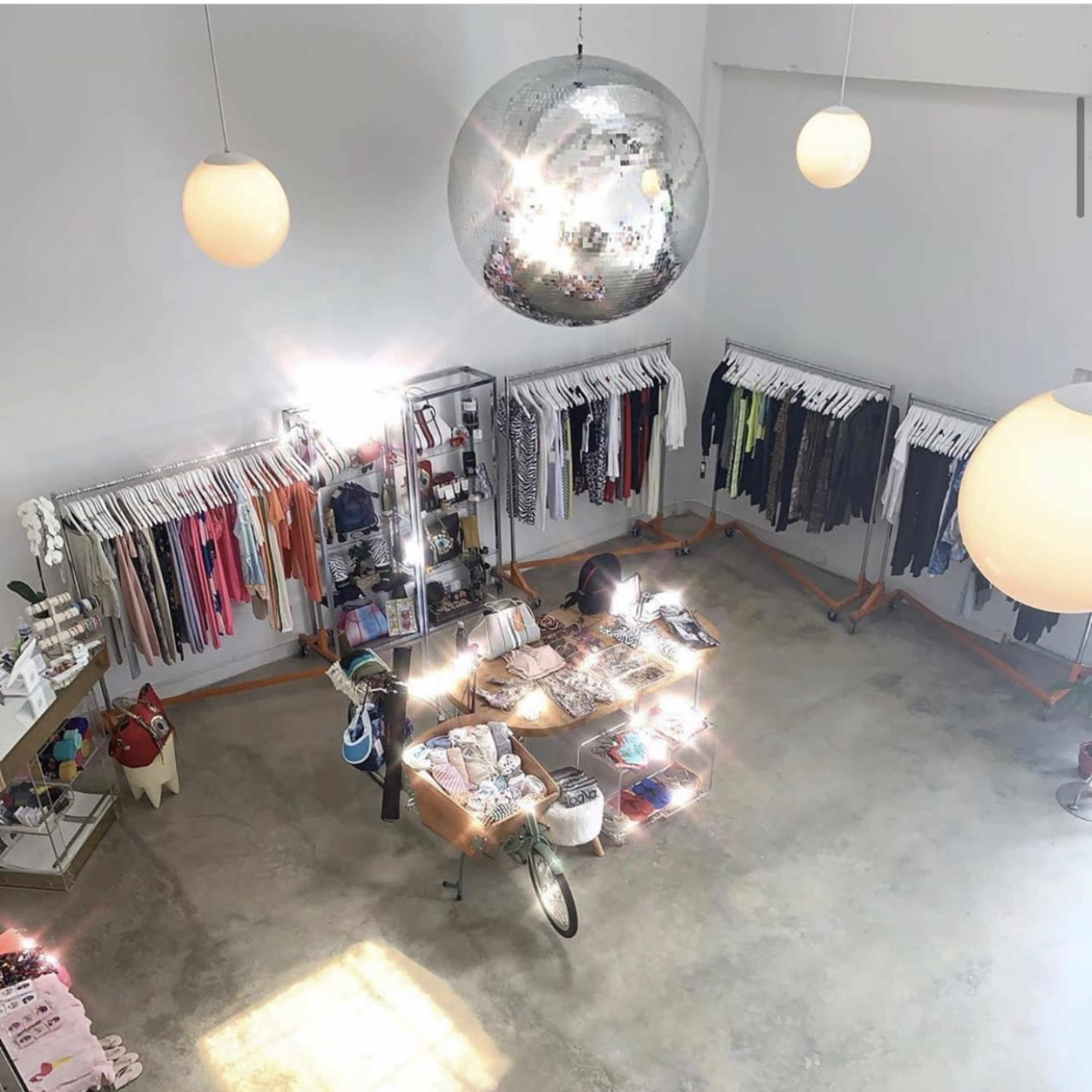 An aerial view of a clothing store with neatly organized apparel on racks and a central display table surrounded by large hanging light fixtures.