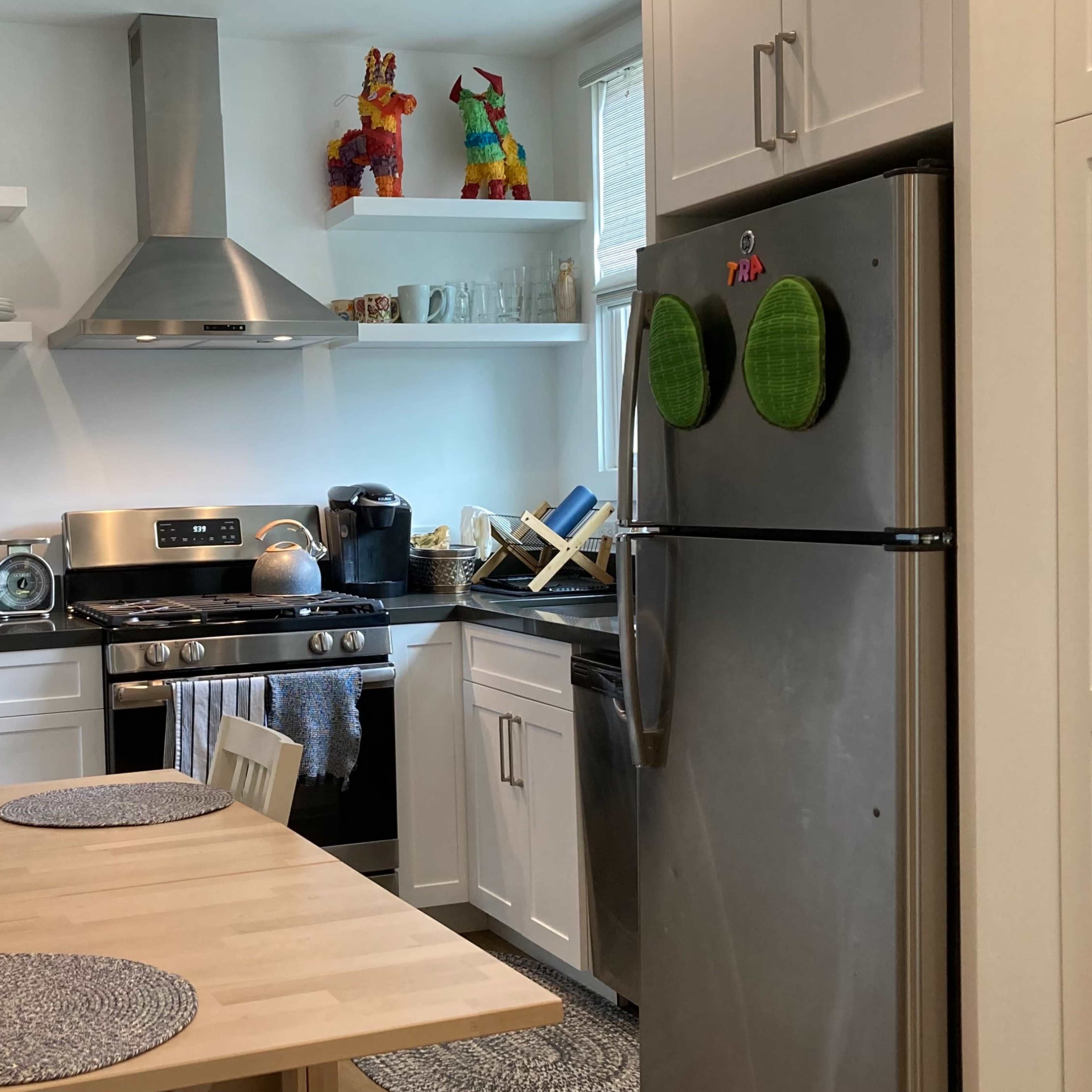 A compact kitchen features stainless steel appliances, white cabinets, and a dining table set for two.