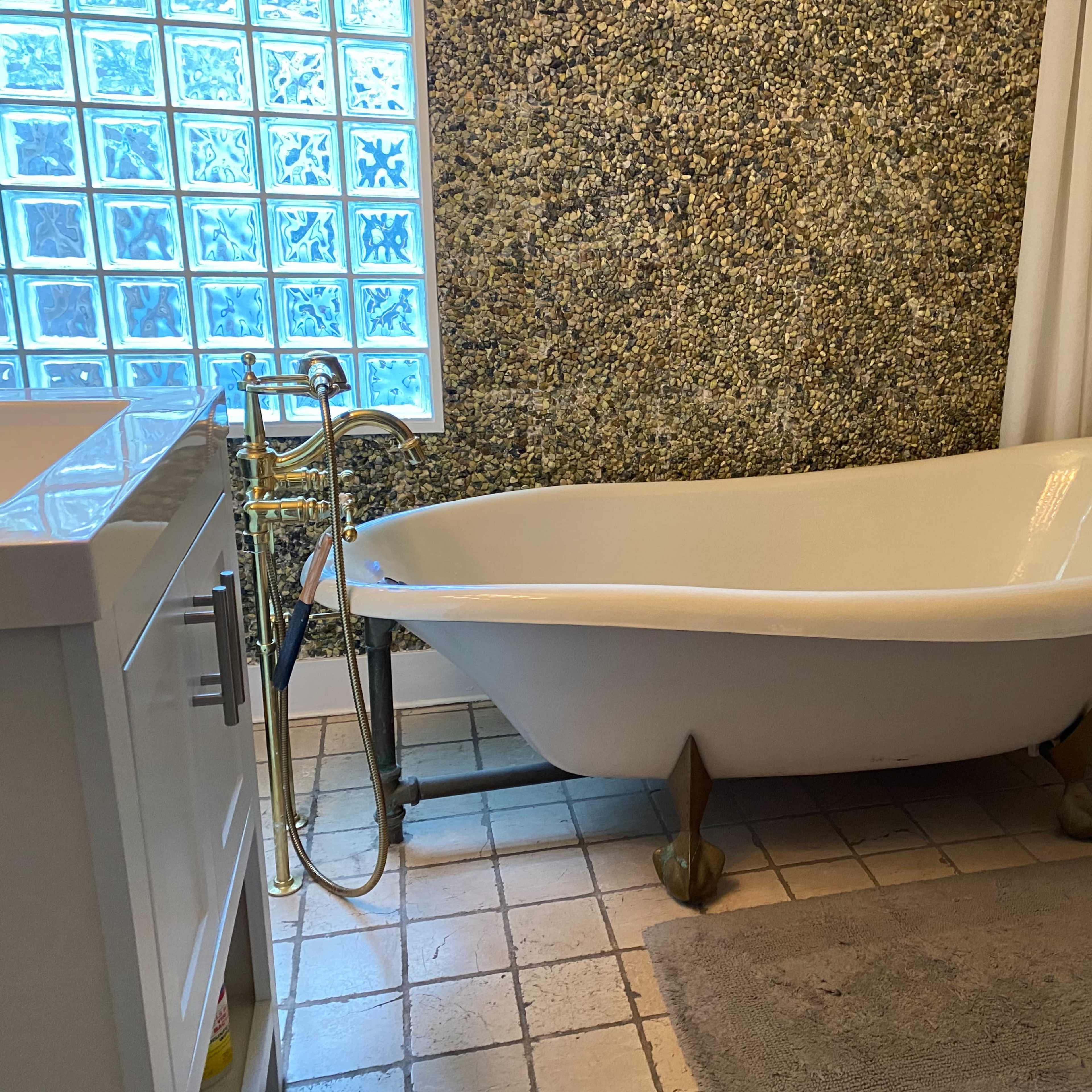 A vintage-style freestanding bathtub next to a window with glass blocks, set in a tiled bathroom.