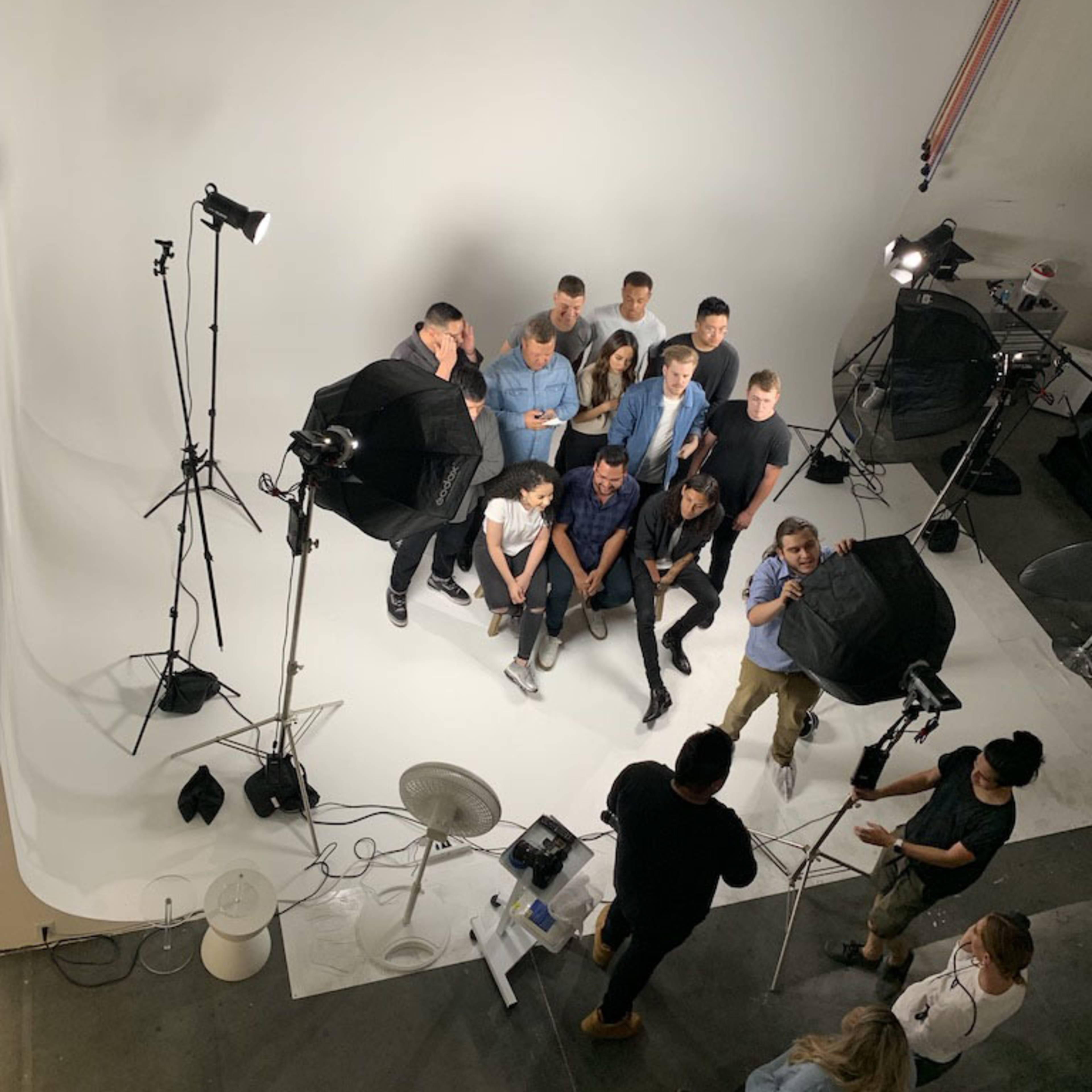 A group of twelve people poses in front of a white backdrop in a photography studio, surrounded by lighting equipment.