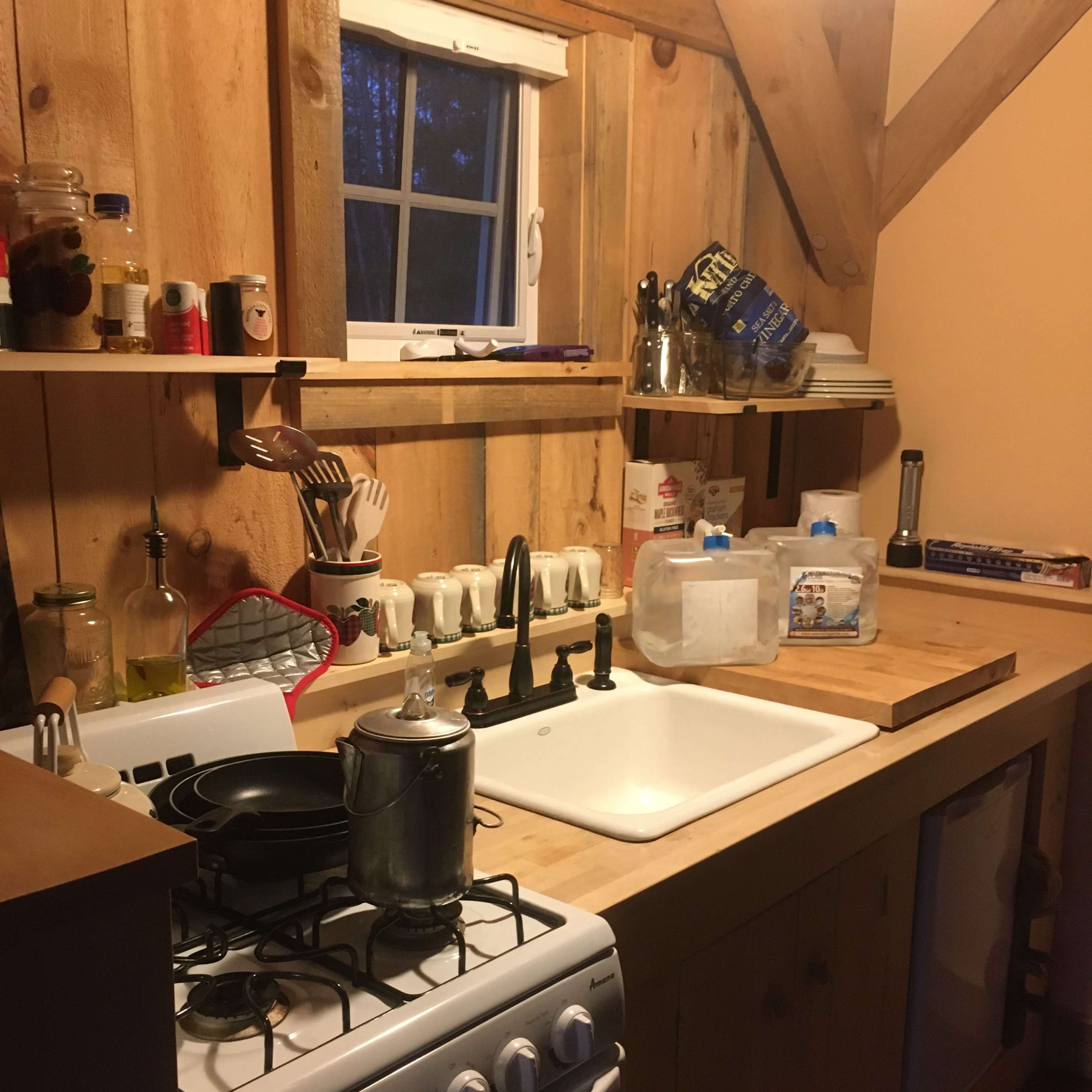 A wooden kitchen with a gas stove, a sink, and organized kitchenware on the countertop.