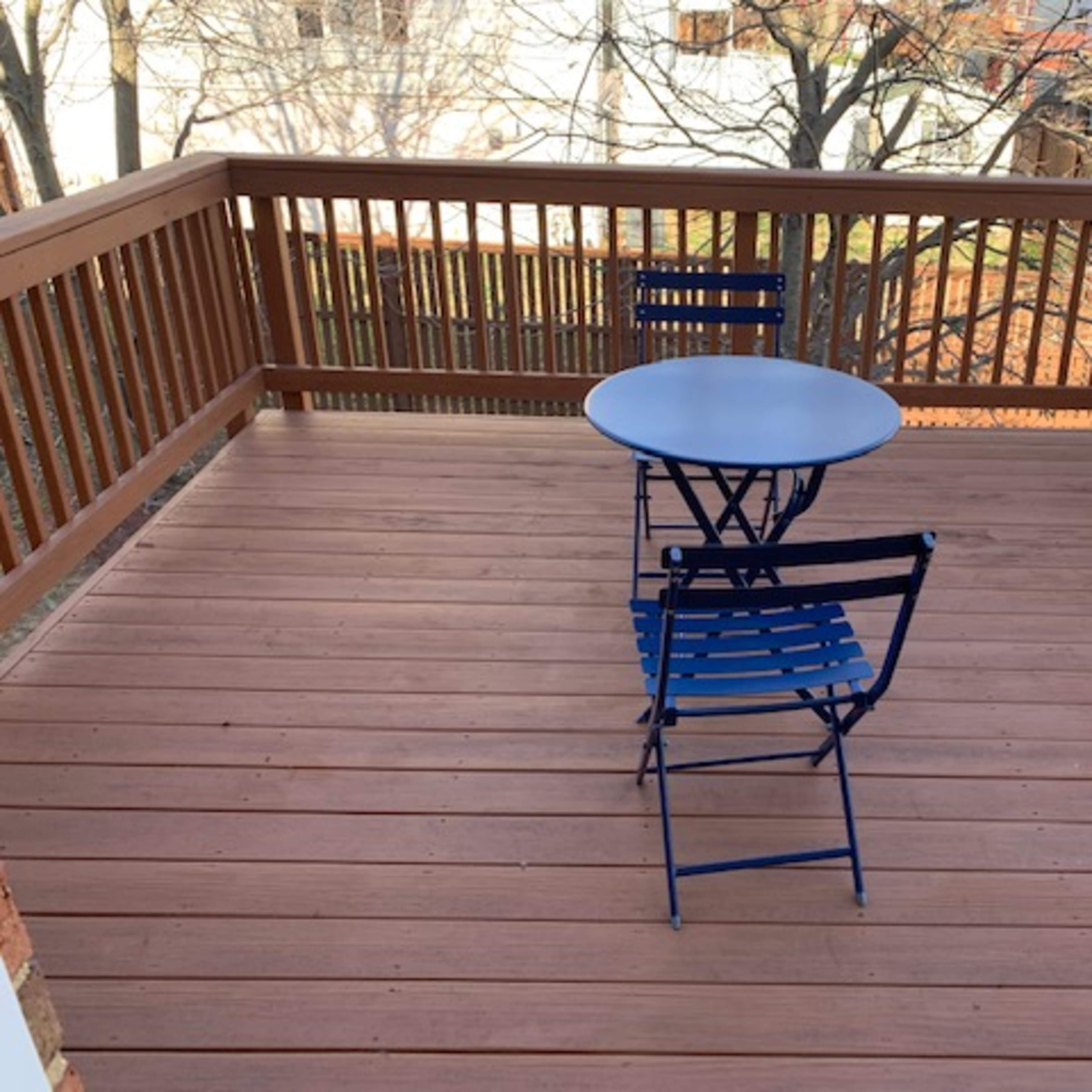 A small deck features a round table and two blue chairs situated in the center.