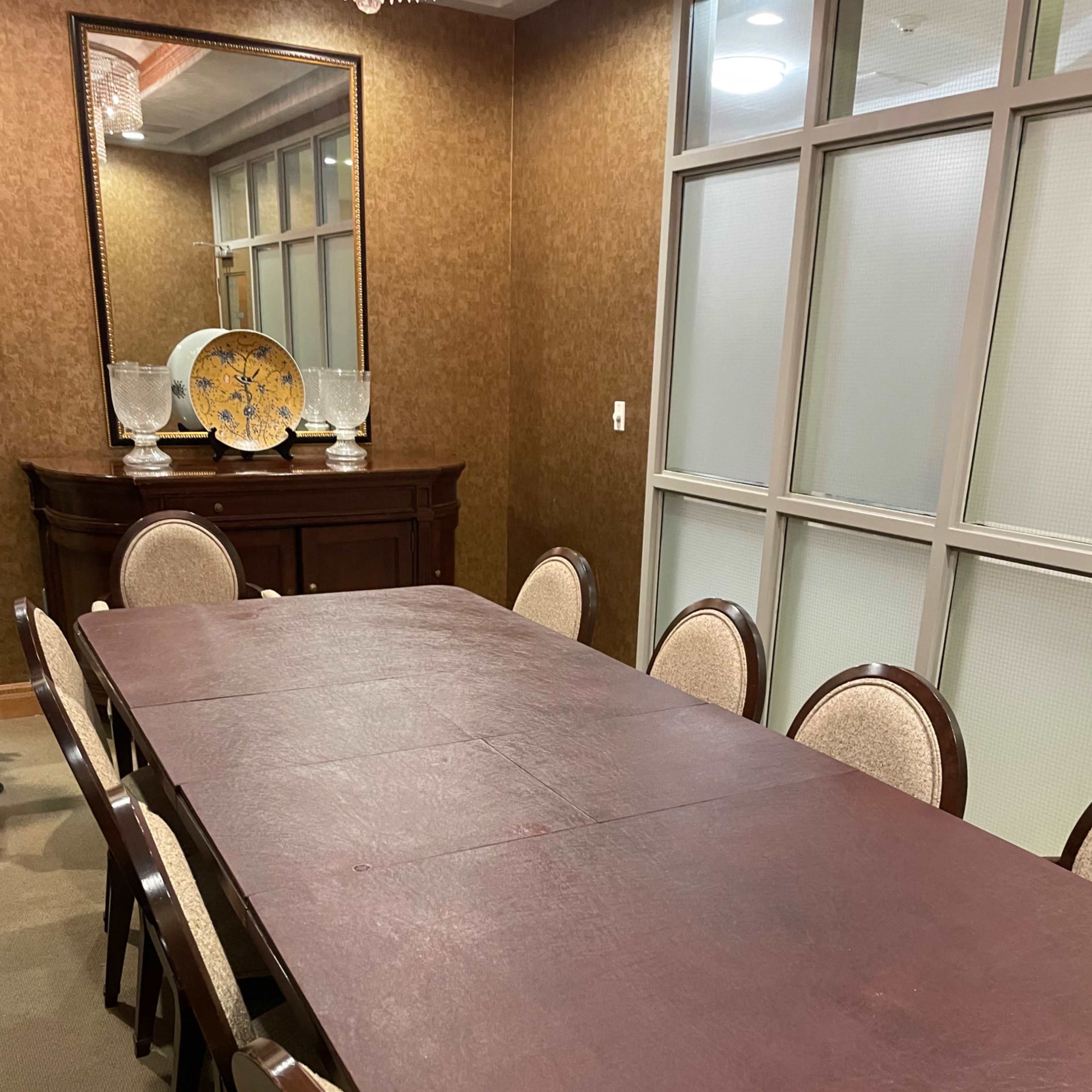A long, rectangular table surrounded by chairs is set in a room featuring brown walls and a large mirror.