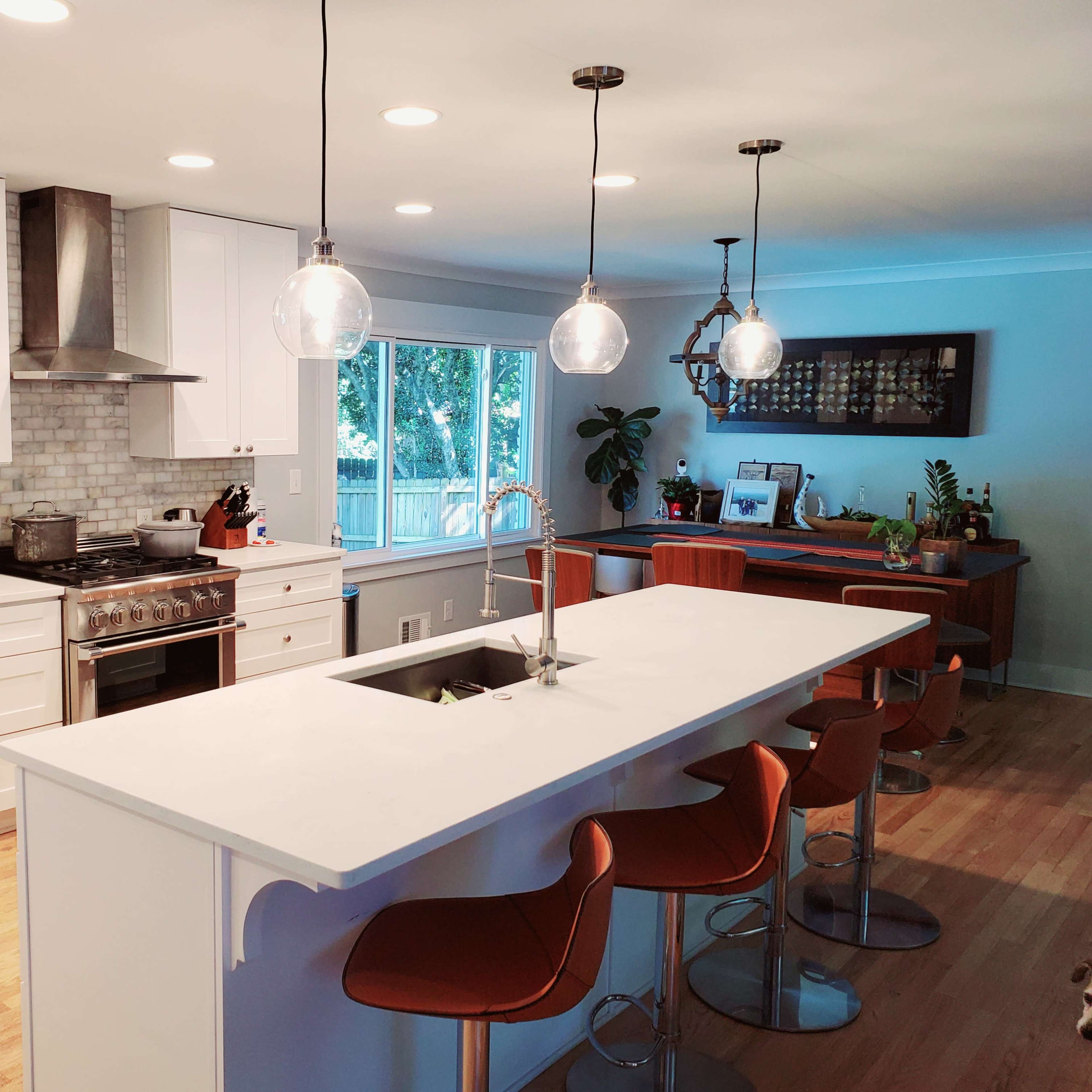 The kitchen features a large island with modern bar stools, stainless steel appliances, and a window overlooking a backyard.