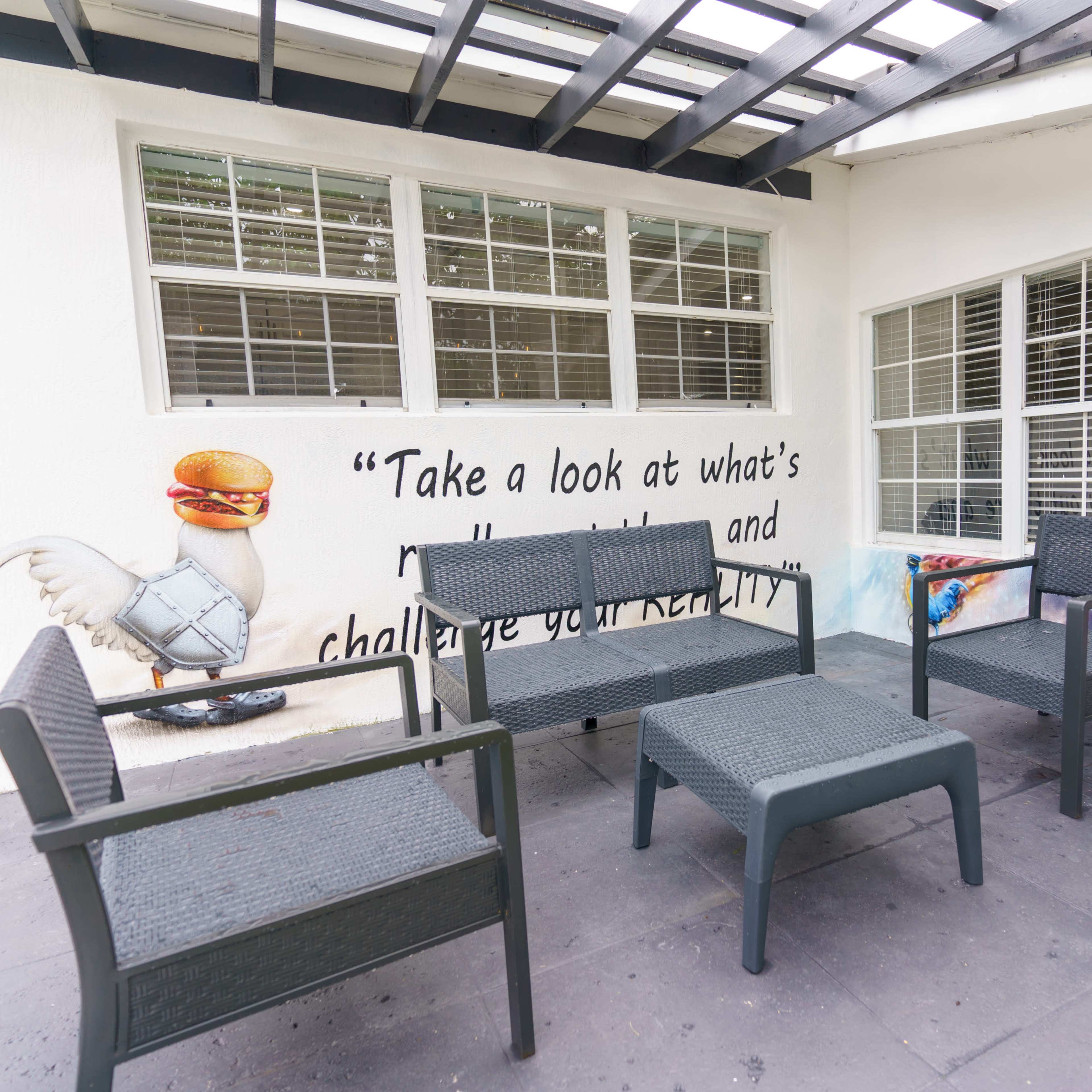 A seating area featuring black wicker chairs and a coffee table is positioned in front of a wall with a mural that includes a quote and a whimsical illustration.