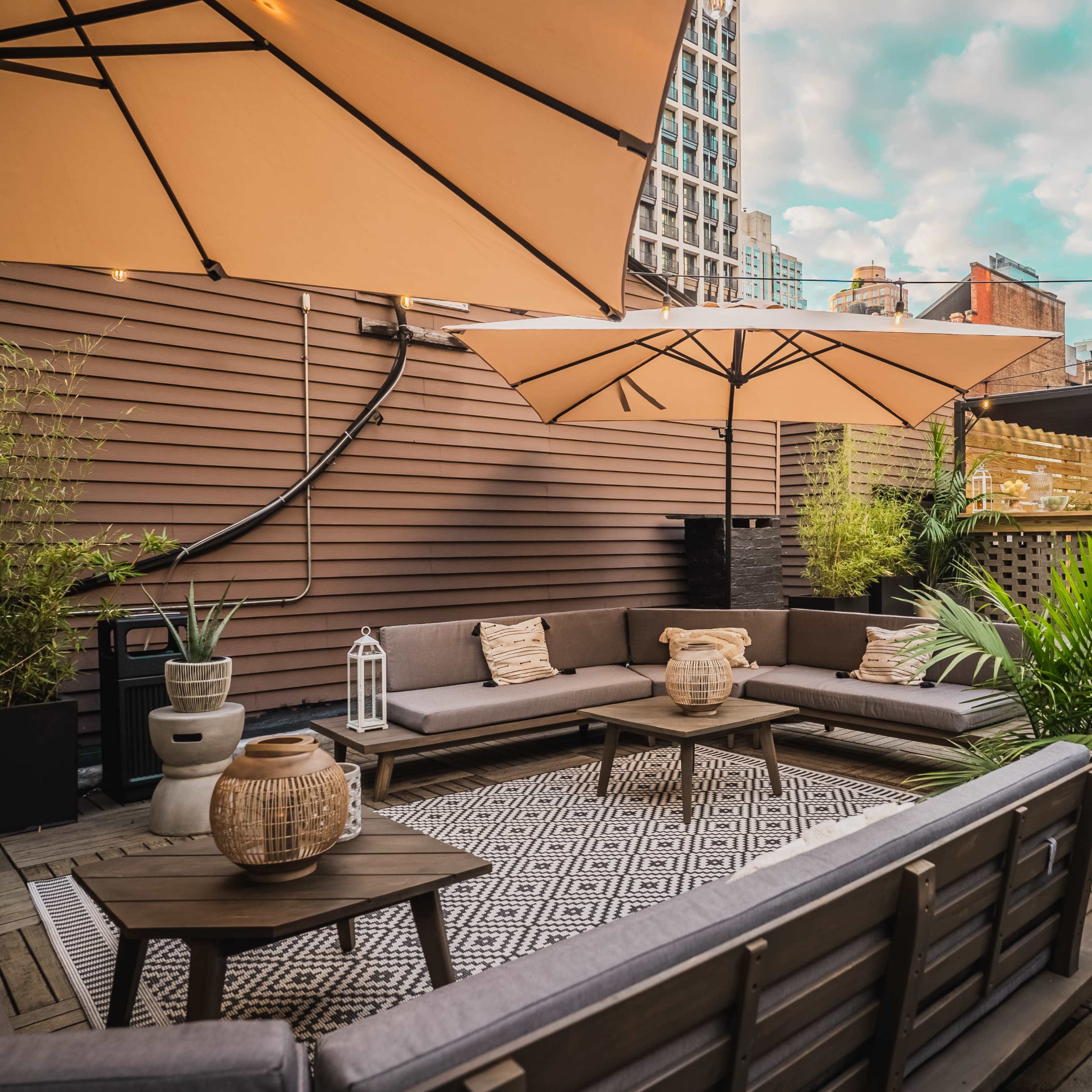 A rooftop patio featuring wooden decking, large umbrellas, modern seating arrangements, and greenery.