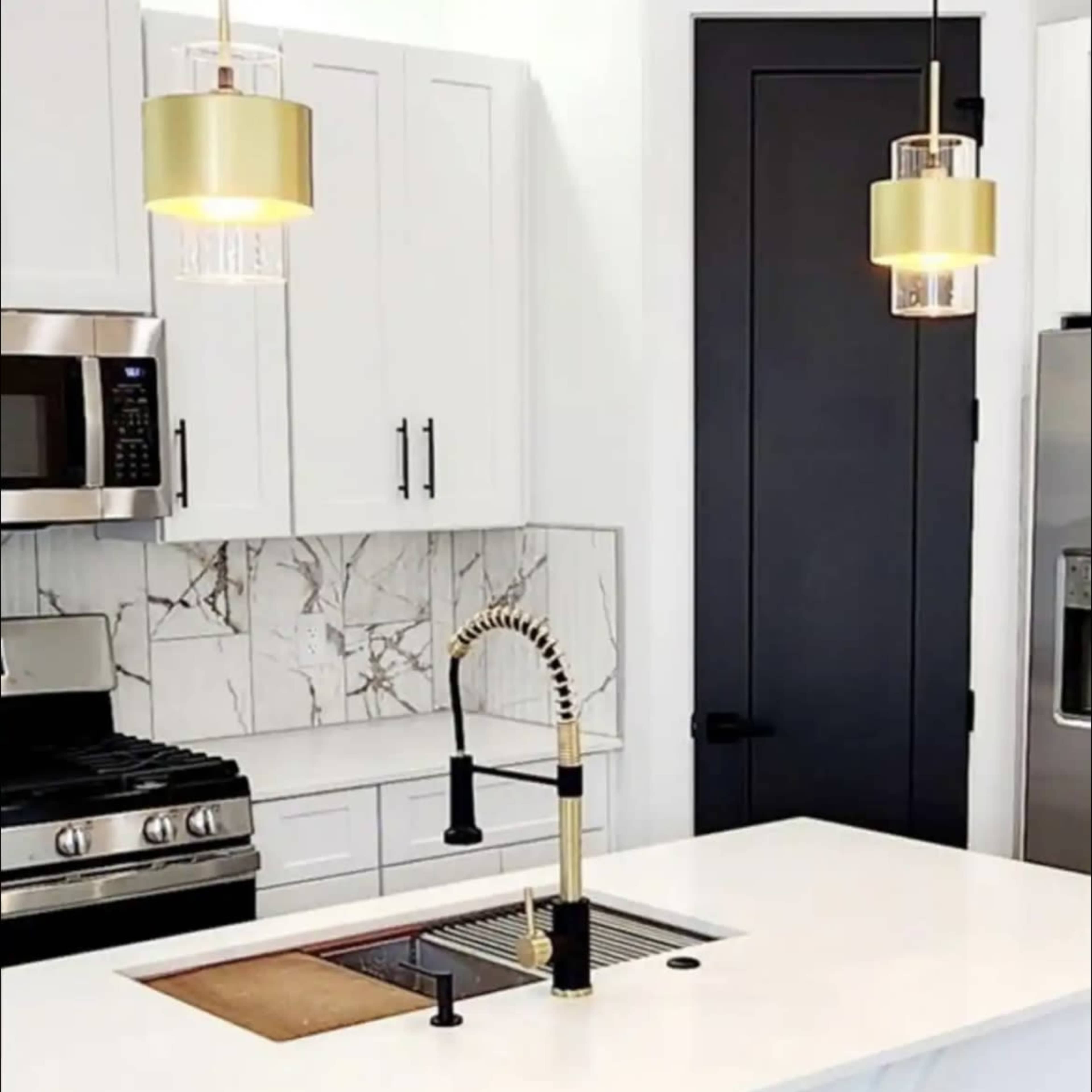 A modern kitchen featuring a stainless steel stove, white cabinetry, a gold-accented faucet, and pendant lights above a white countertop.