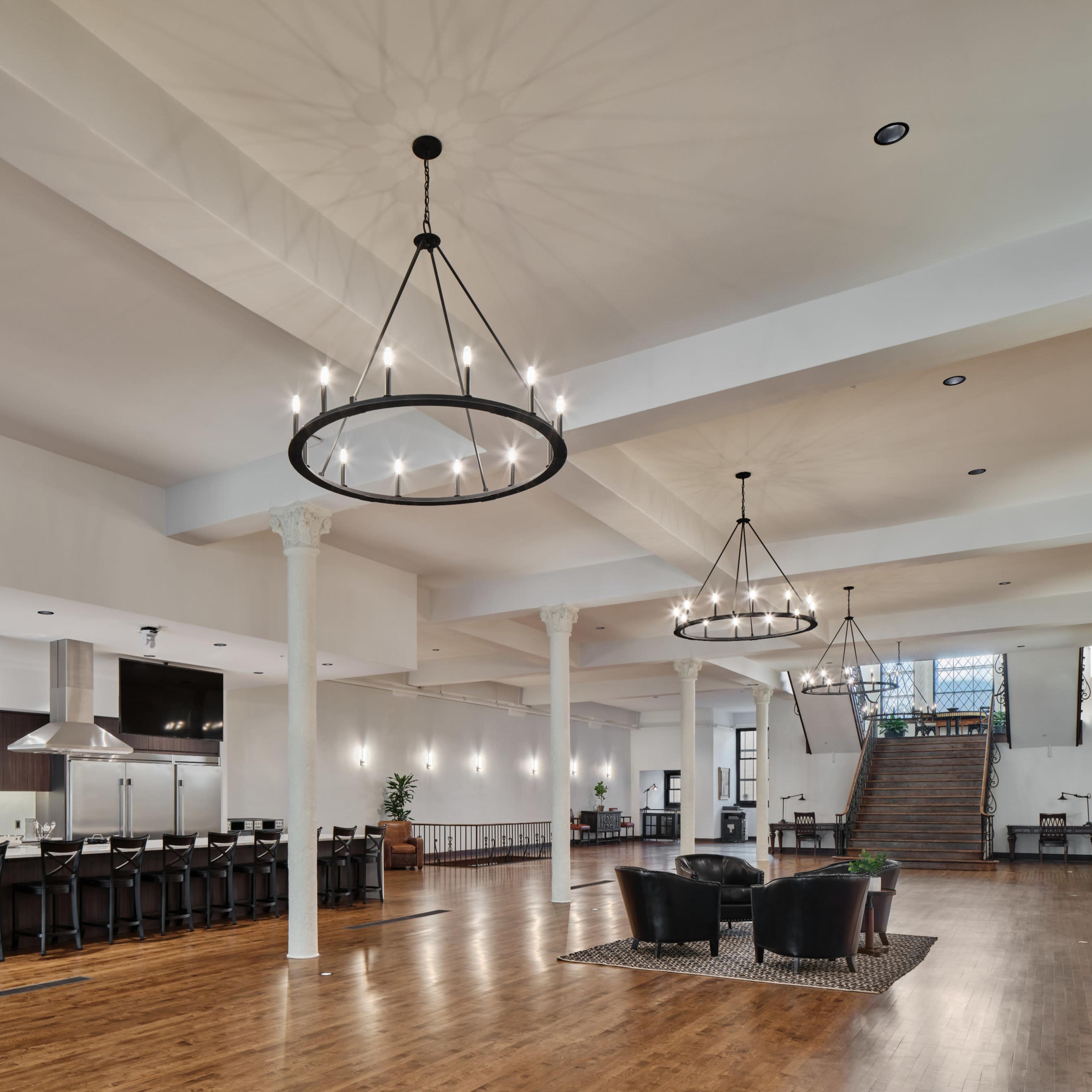 A spacious interior with wooden flooring, a large bar area, and two circular chandeliers hanging from the ceiling.