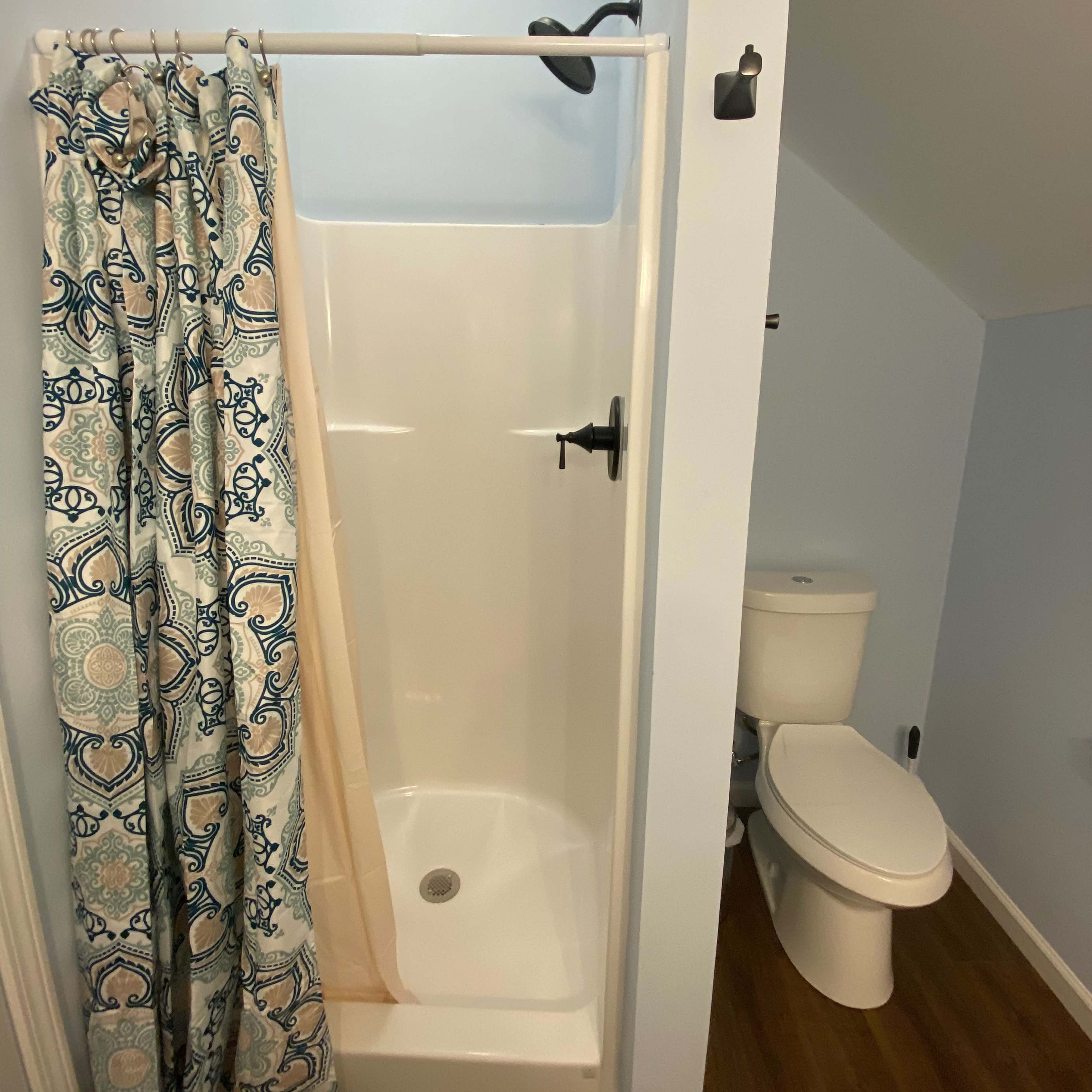 A small bathroom featuring a shower stall with a patterned curtain and a toilet adjacent to it, all under a sloped ceiling.