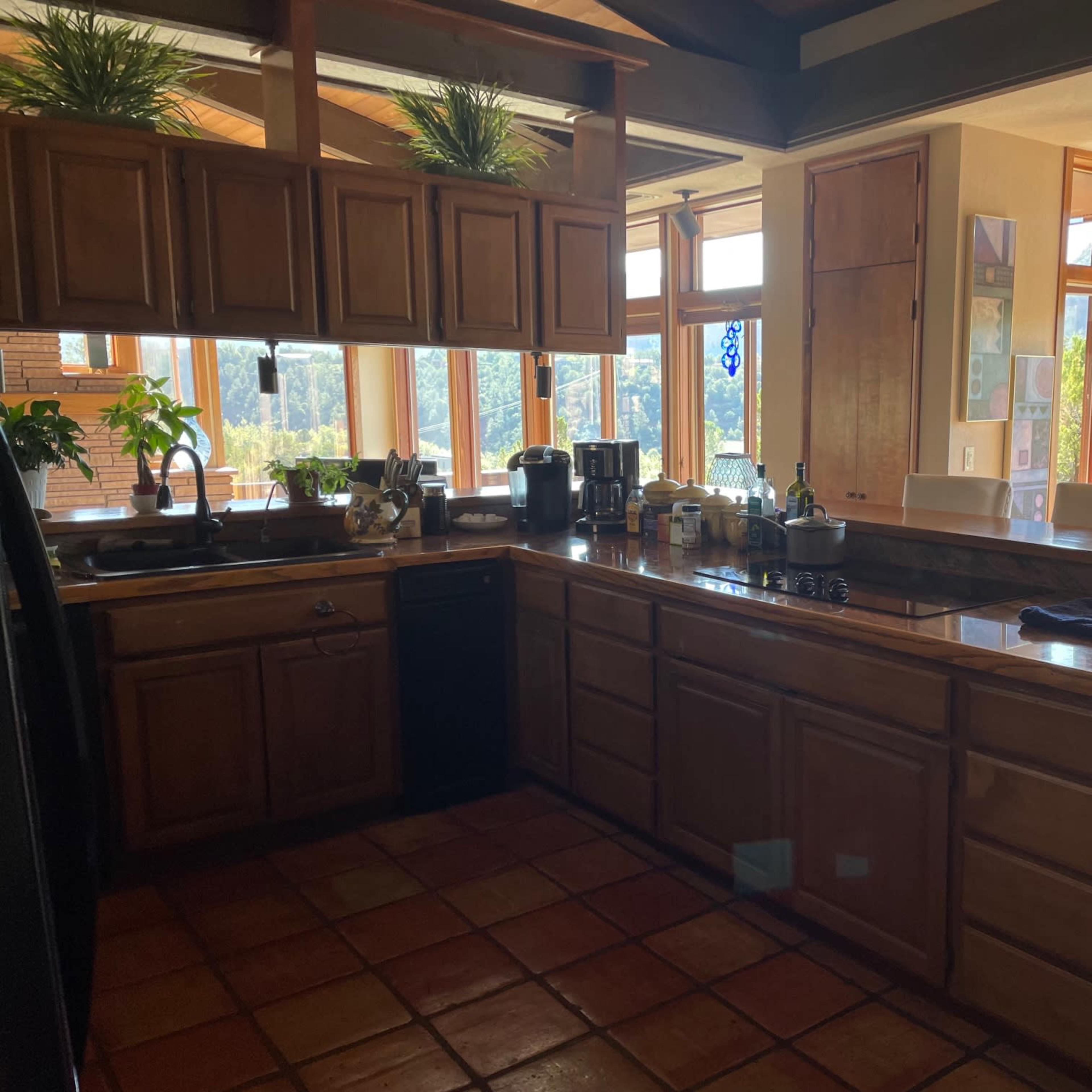 A spacious kitchen with wooden cabinetry, a dark countertop, and large windows that provide natural light.