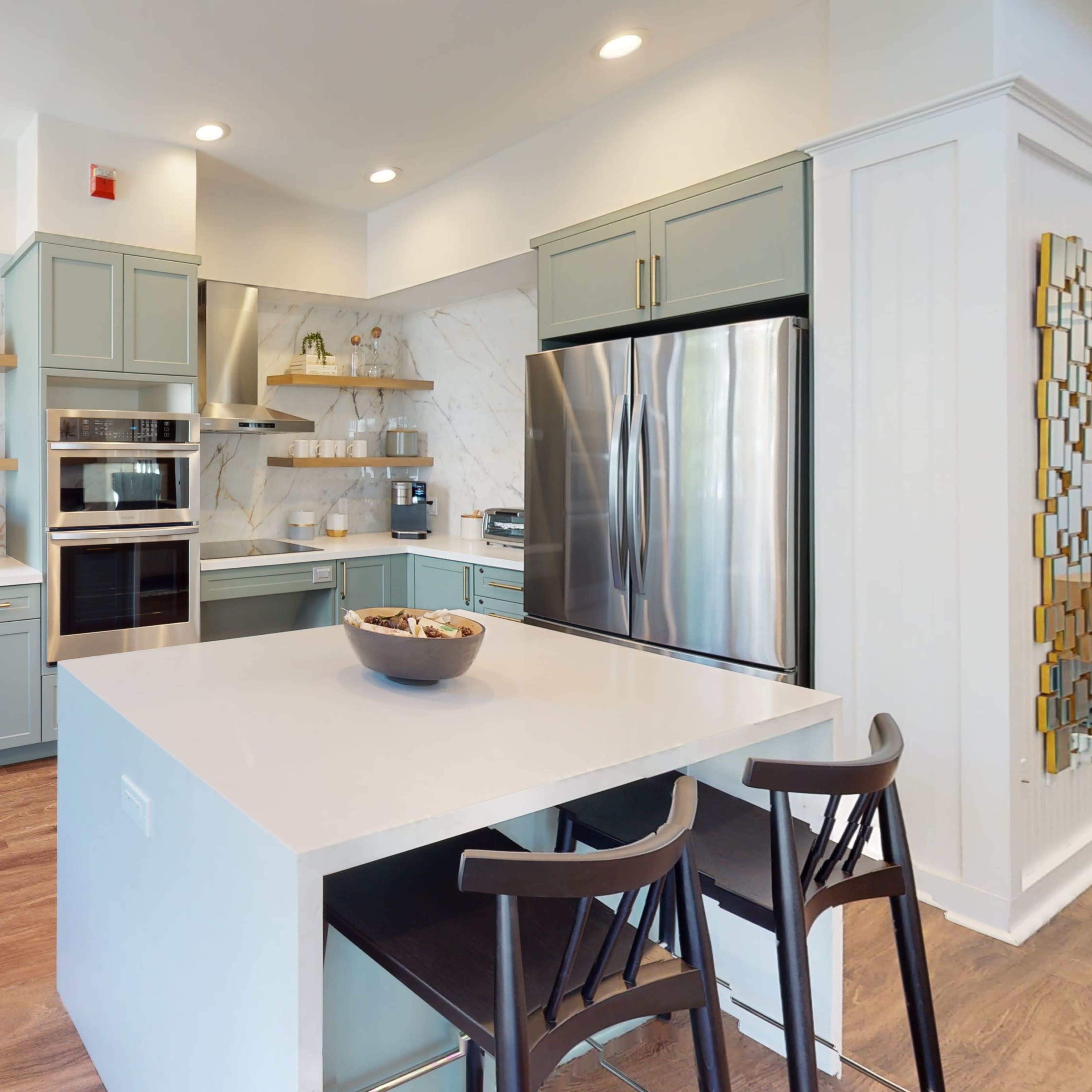 A modern kitchen featuring light green cabinetry, stainless steel appliances, and a large island with bar stools.