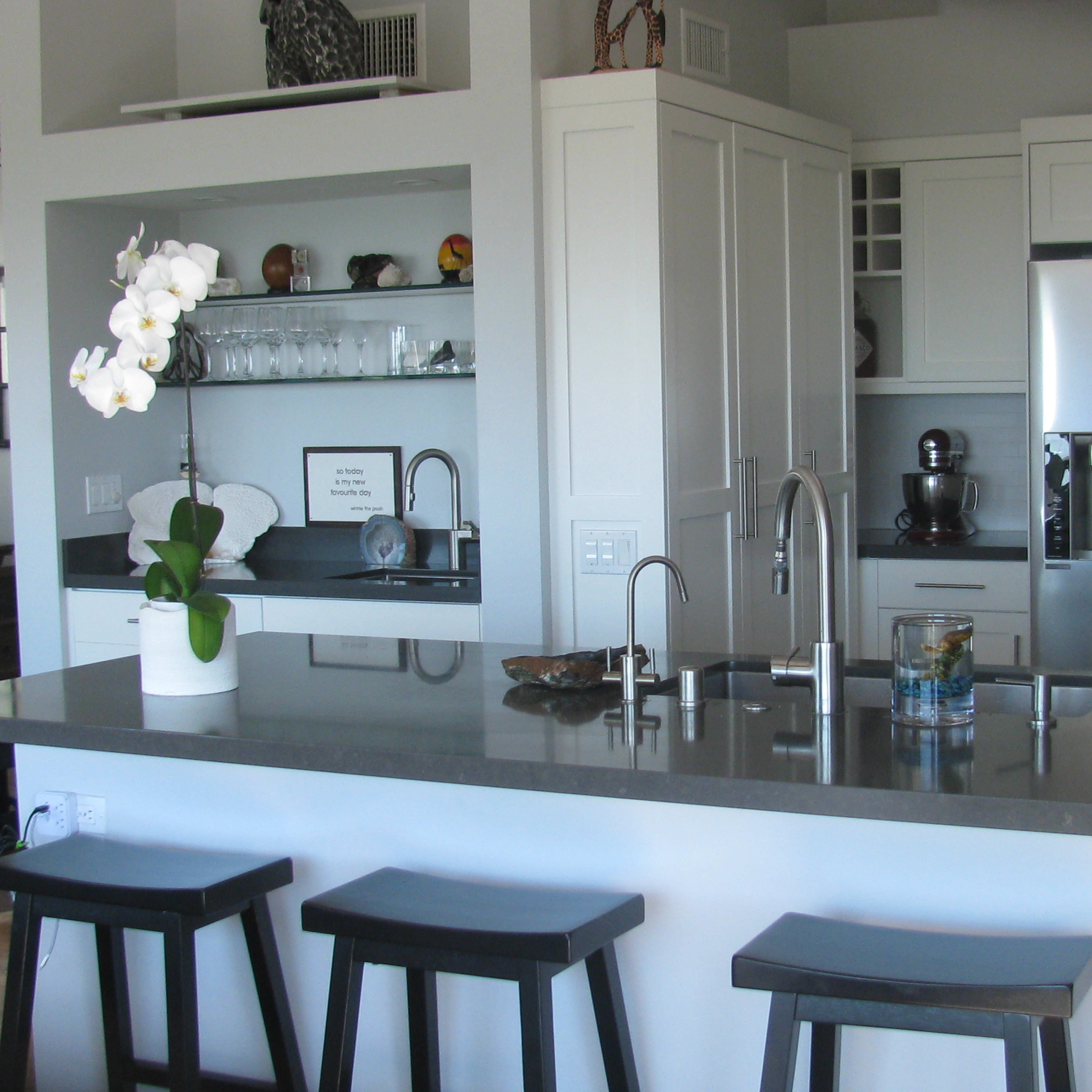 A modern kitchen with a large island, sleek appliances, and a small dining area visible in the background.