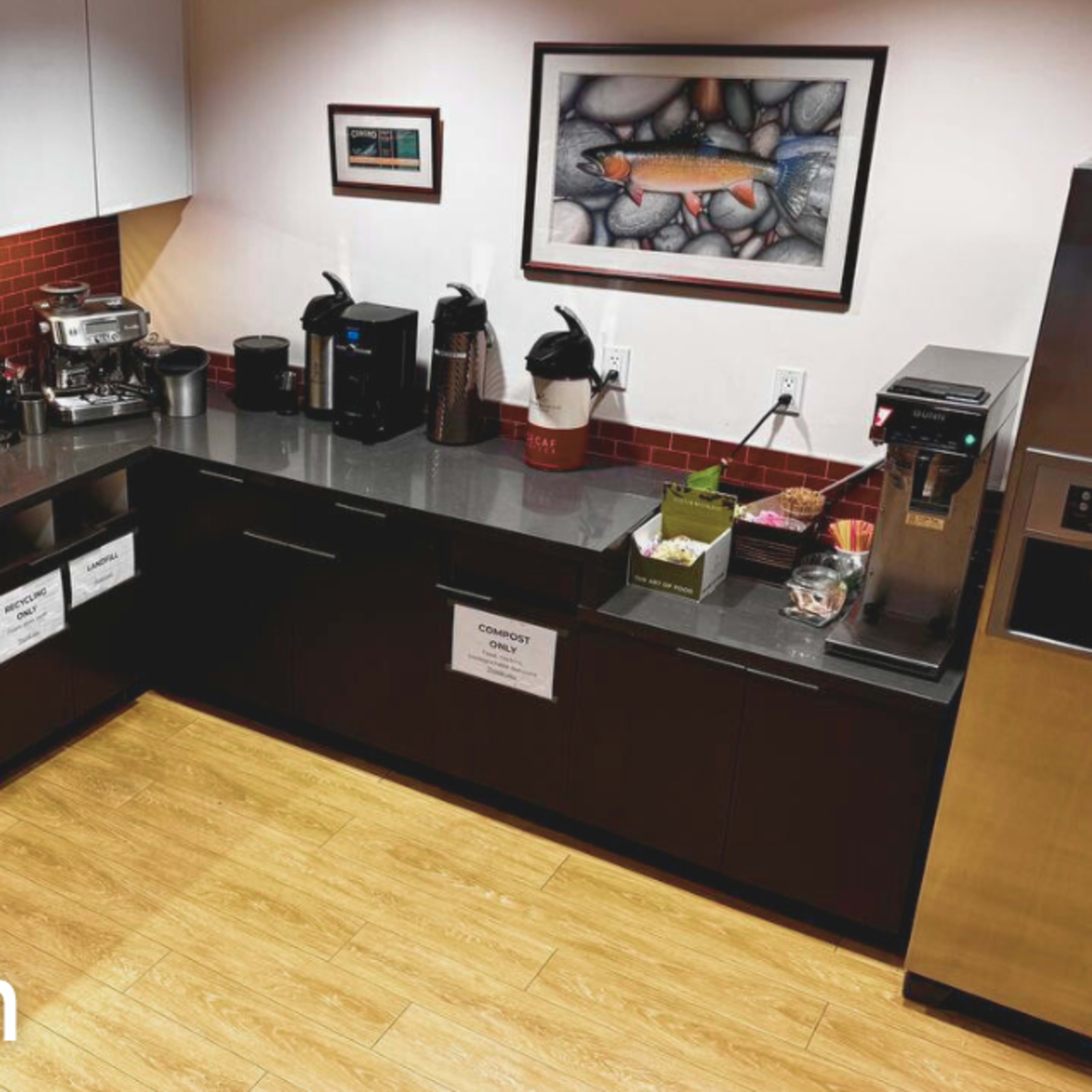 A coffee station in a kitchen with a sink, microwave, coffee machines, and various utensils on a black countertop.
