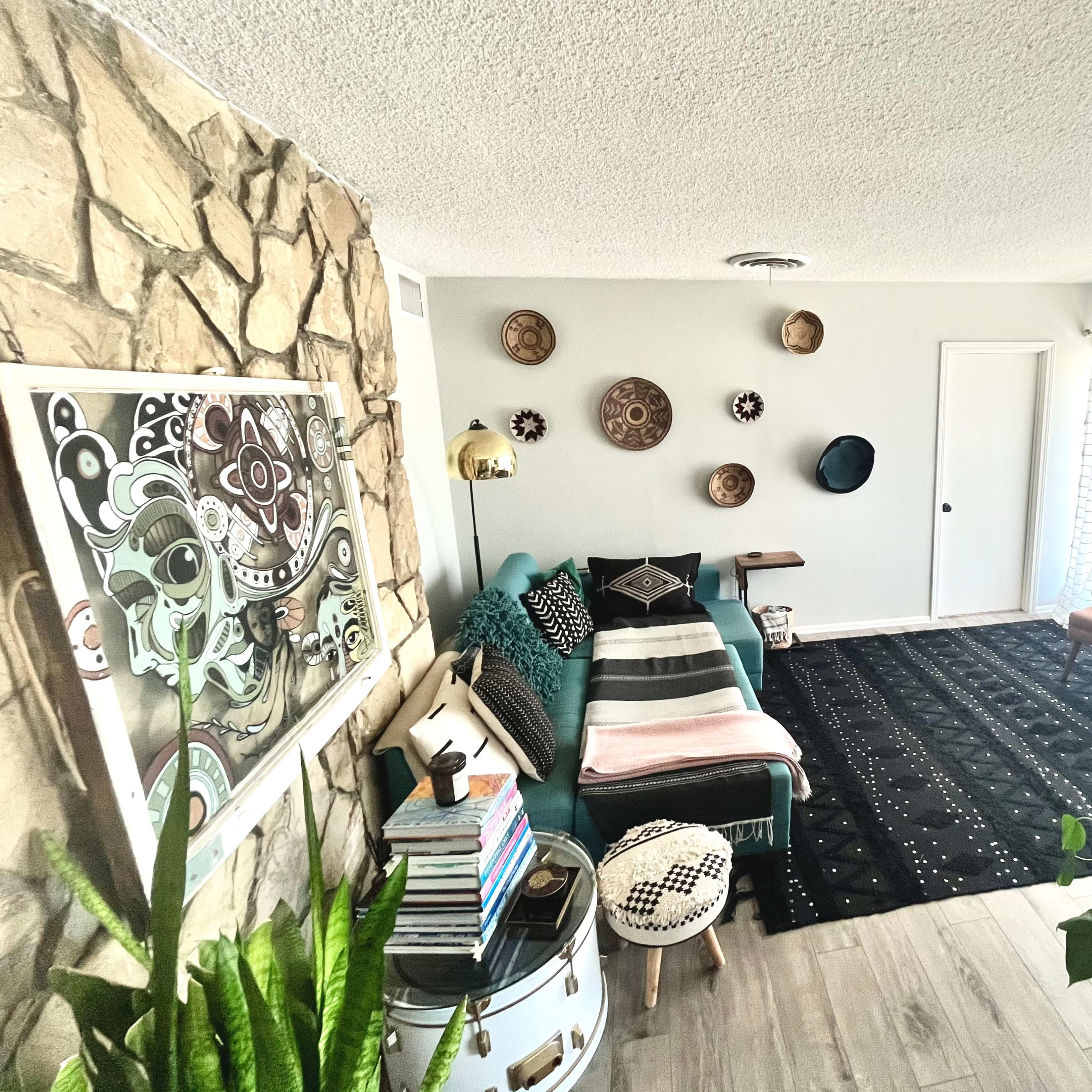 A modern living room featuring a stone accent wall, a teal sofa, an area rug, and various decorative wall plates.