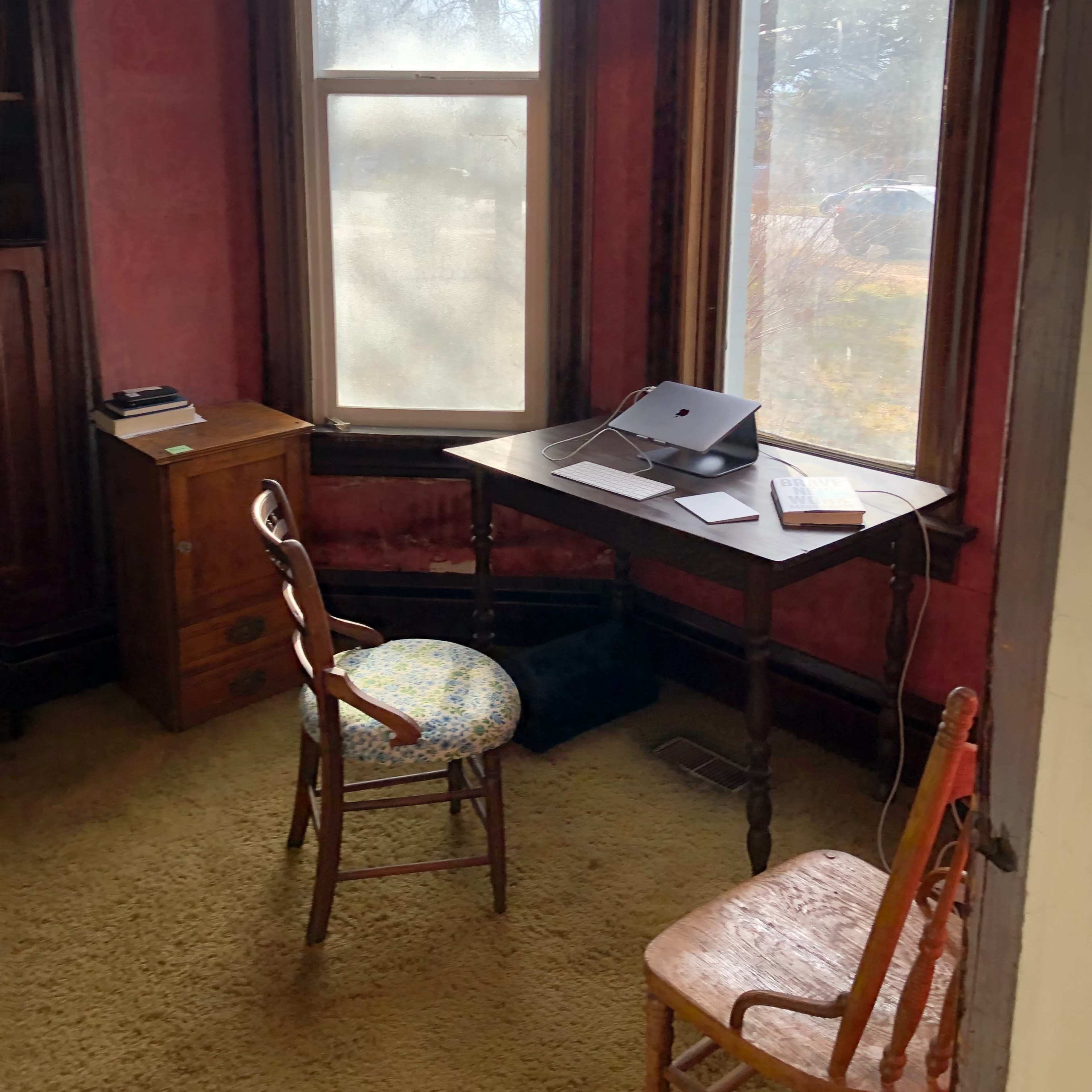 A small room with a table, two chairs, a laptop, and large windows that allow natural light in.