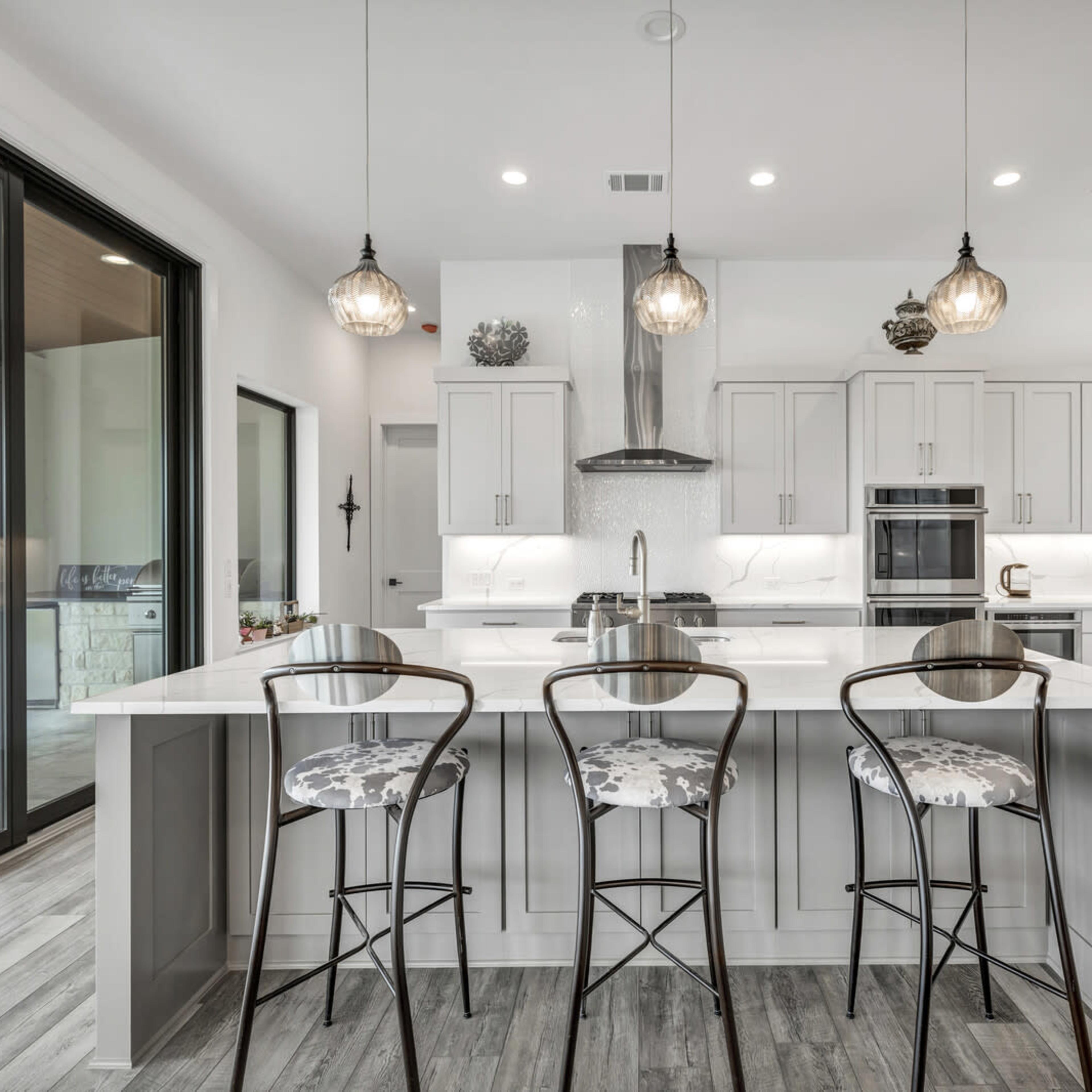 A modern kitchen features white cabinetry, a large island with seating for three, and large windows that provide natural light.