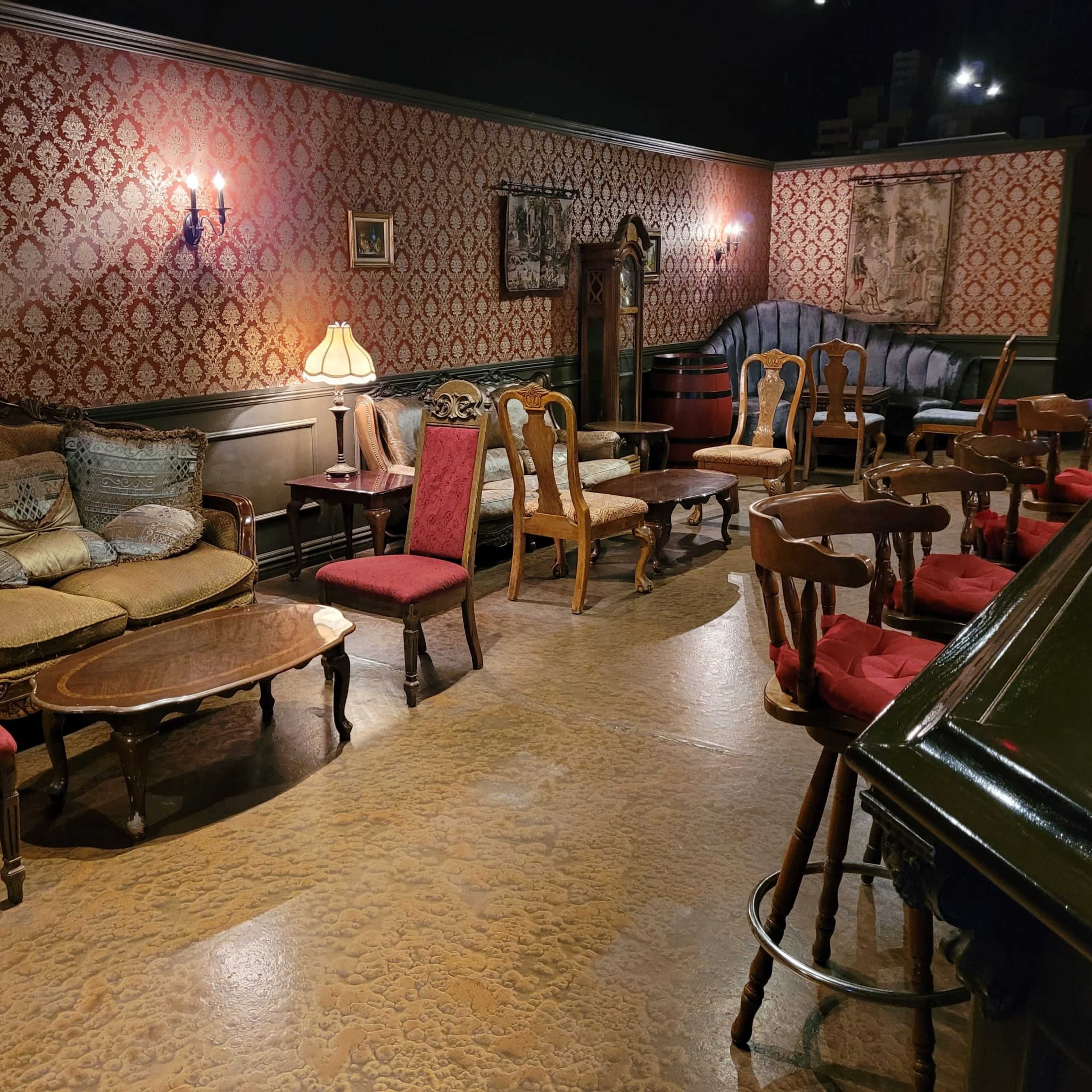 A vintage-style seating arrangement in a dimly lit room with patterned wallpaper and various chairs and tables.