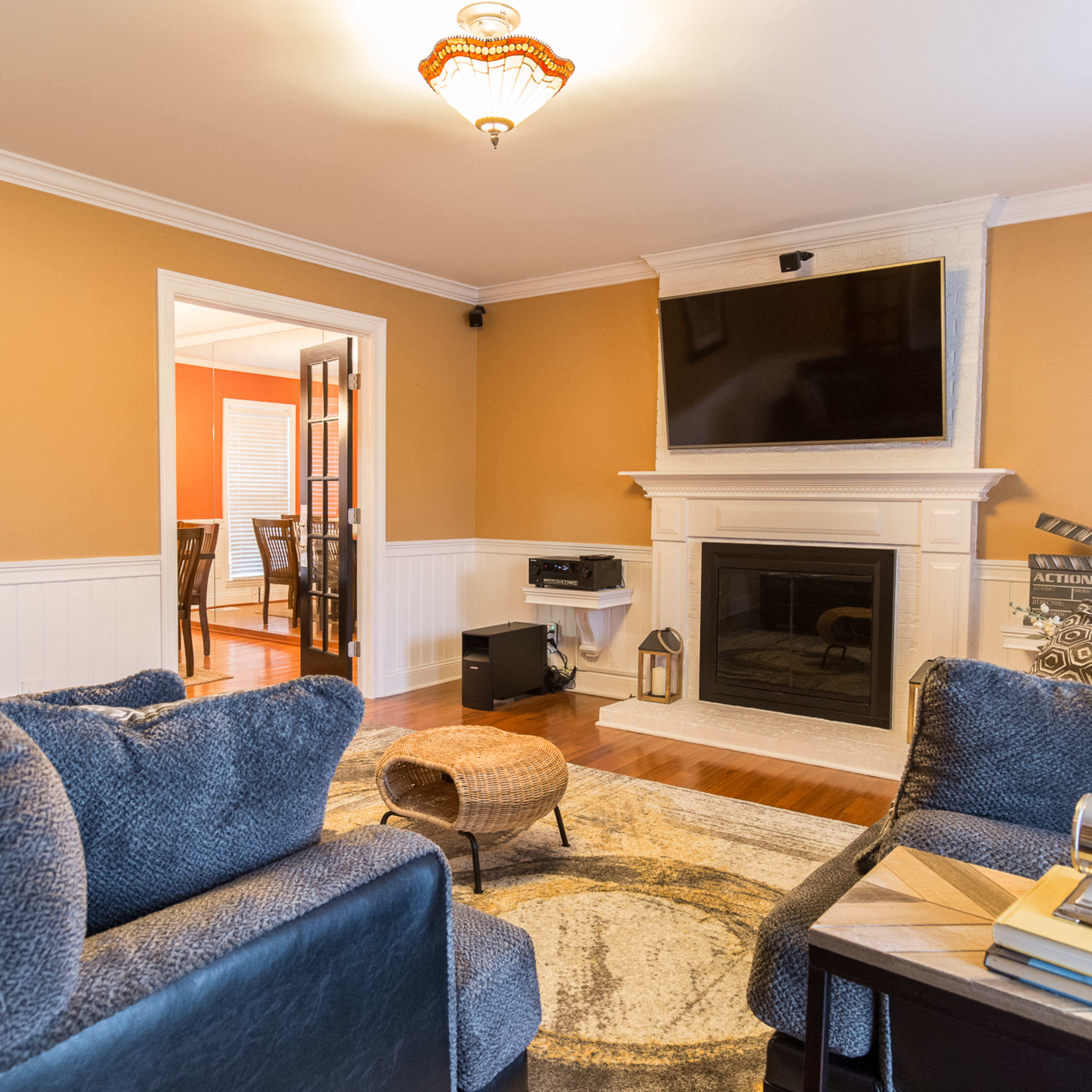 A cozy living room features two dark sofas, a fireplace with a mounted television above it, and an entrance to a dining area in the background.