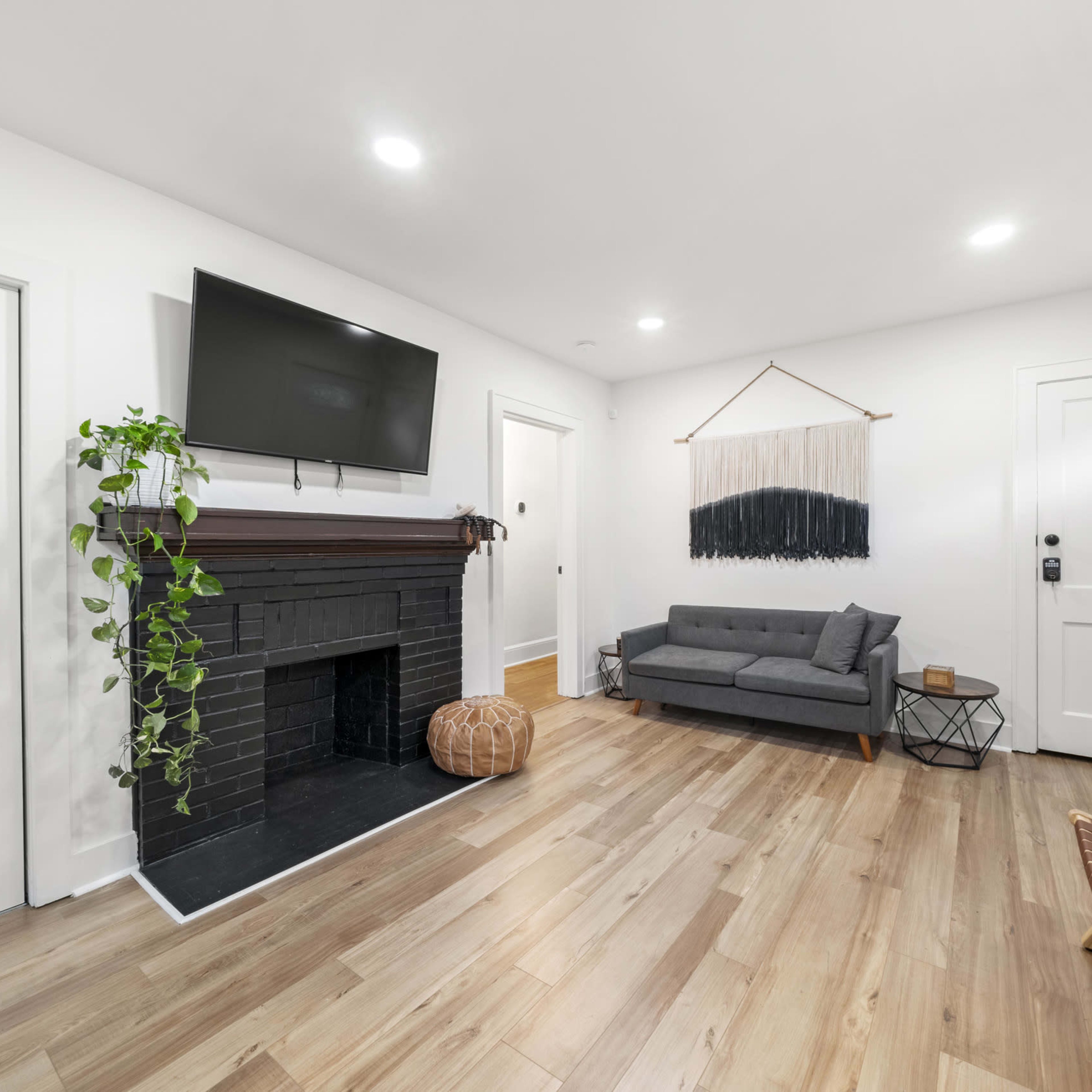 The living room features a black fireplace with a television above, a gray sofa, a small geometric coffee table, and hardwood flooring.