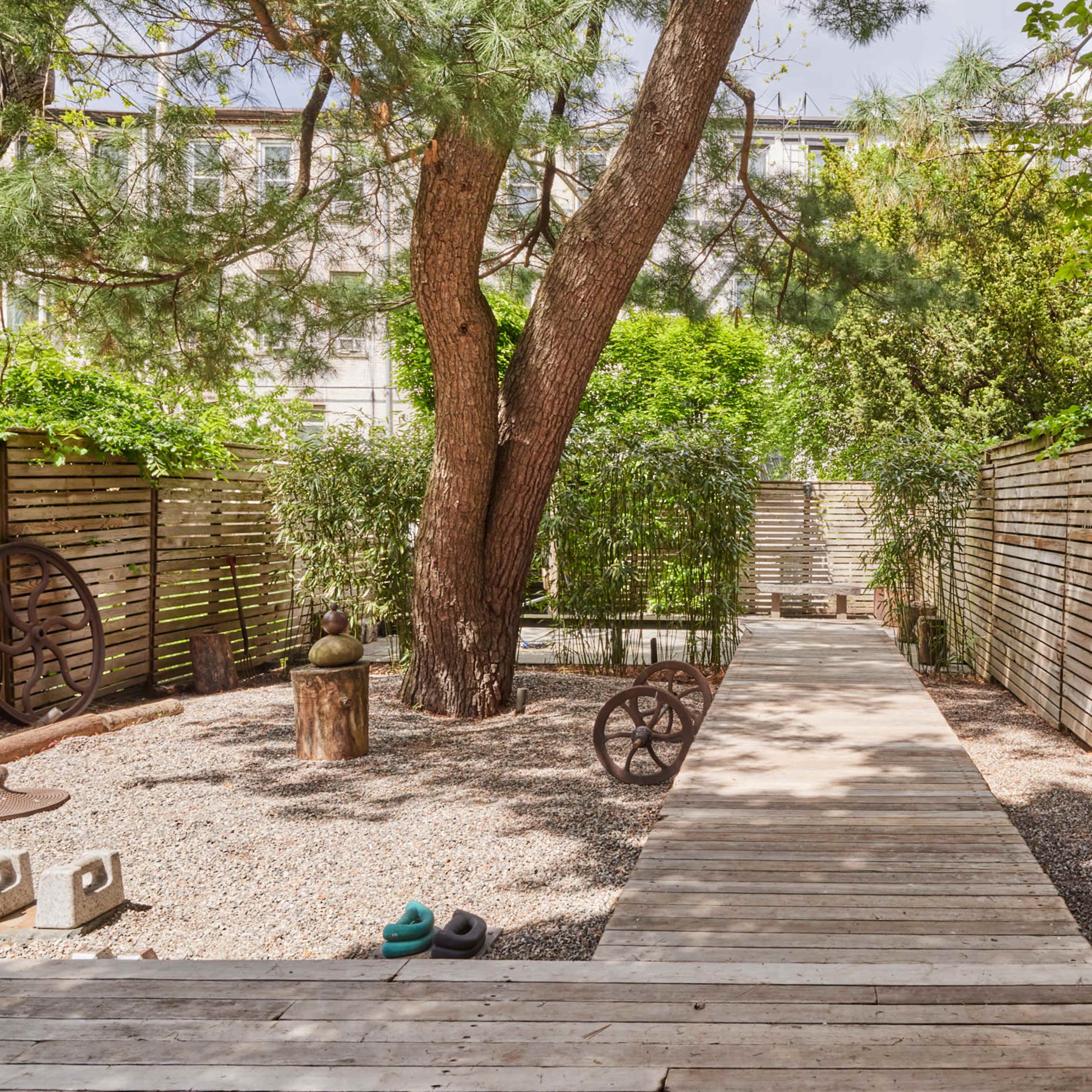A wooden pathway runs between tall trees and wooden fences in a landscaped garden.