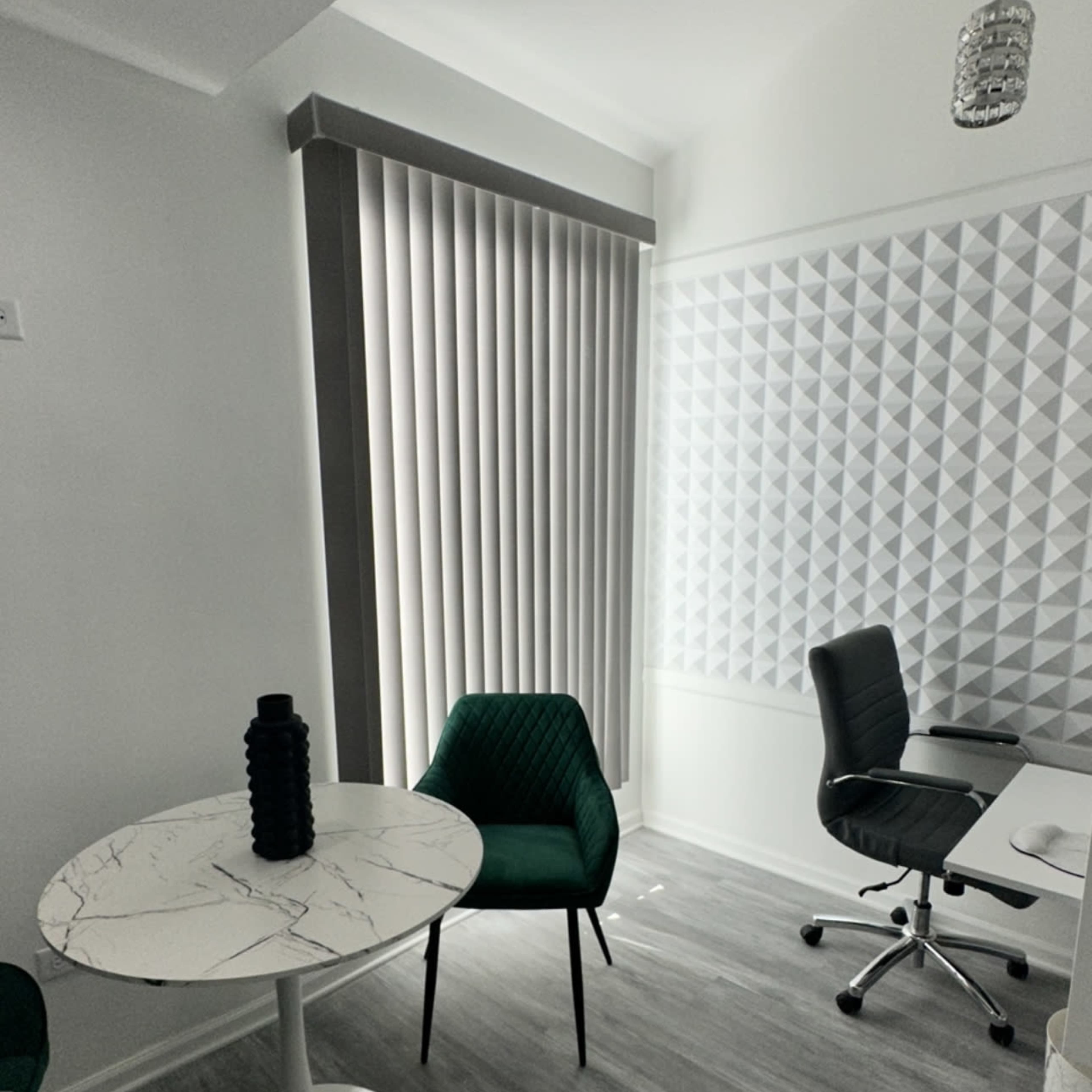 A modern office space featuring a round marble table, two chairs, and a wall with a textured panel design.