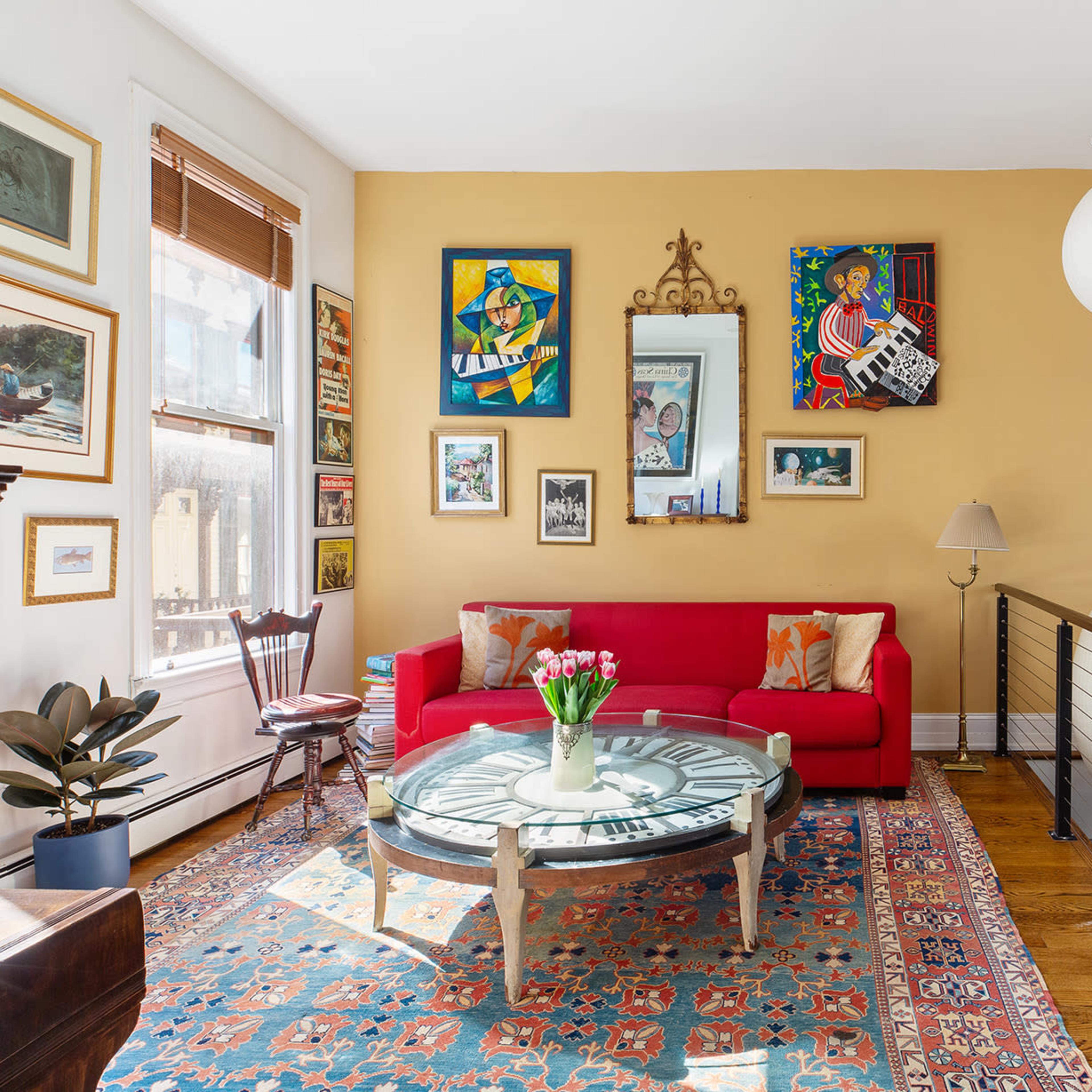 A well-lit living room featuring a red sofa, glass coffee table, and walls adorned with various framed artworks.