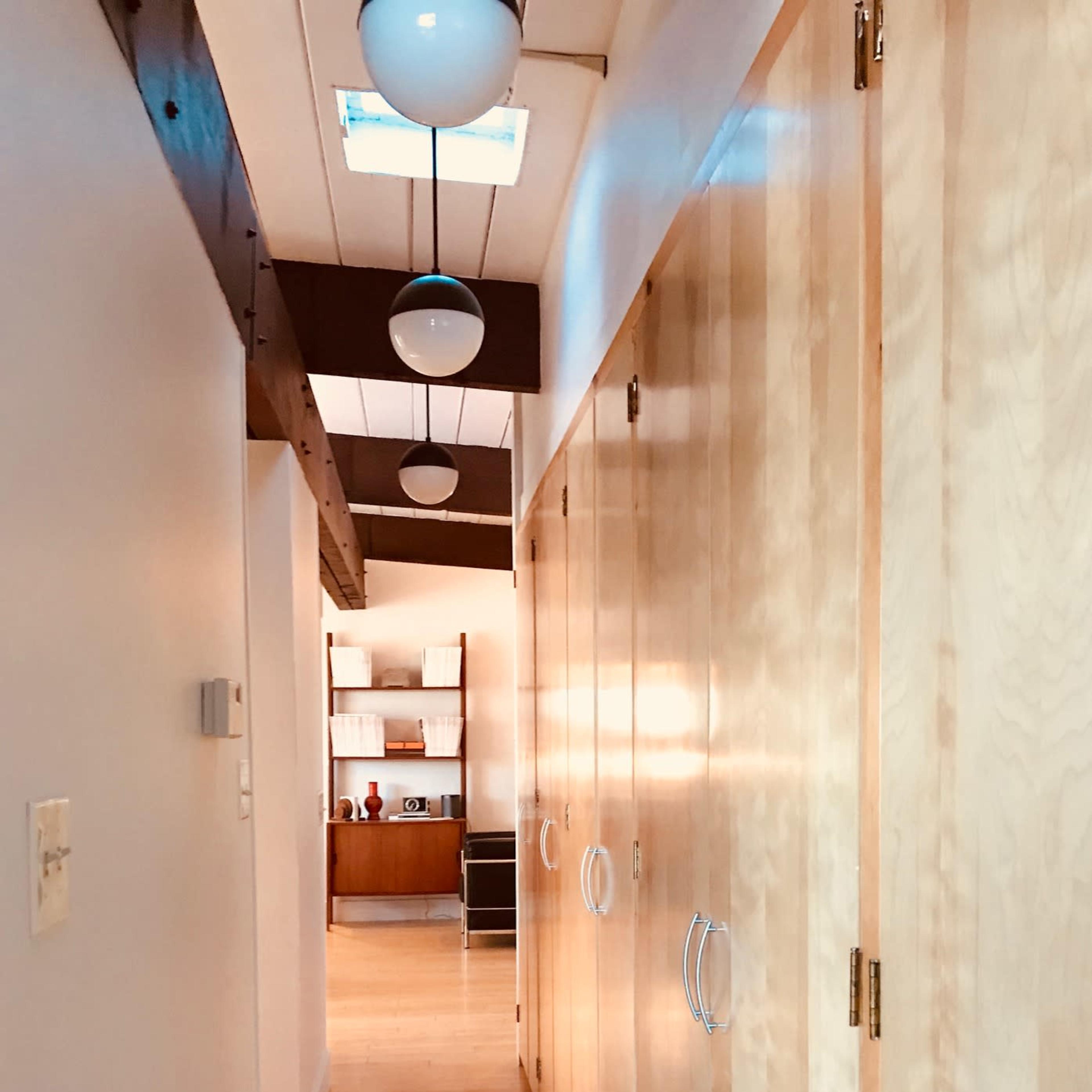 A long hallway features wooden cabinets on one side and a view of a room at the end, illuminated by pendant lights above.