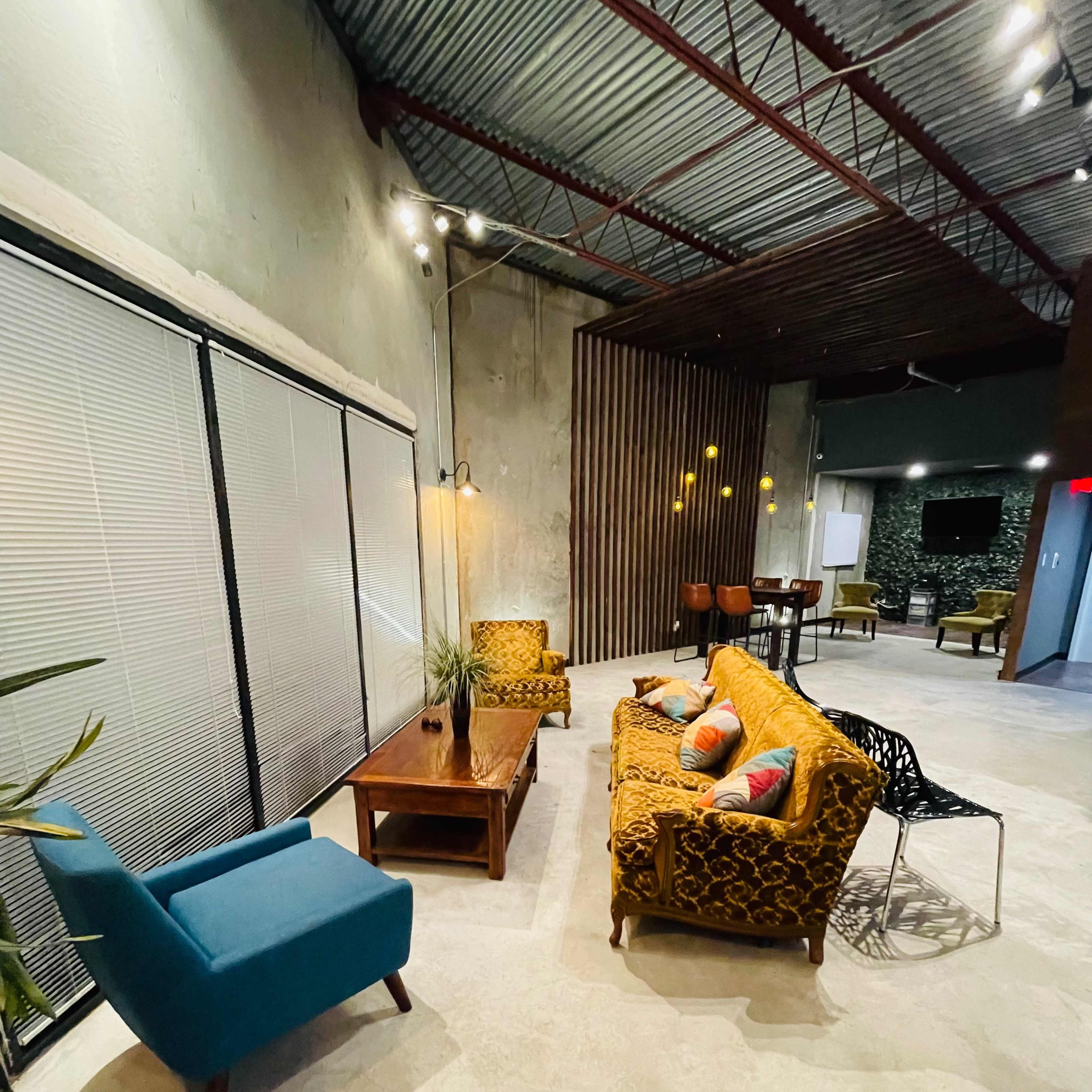 A modern lounge area features a mix of colorful seating, a wooden coffee table, and large windows with blinds.