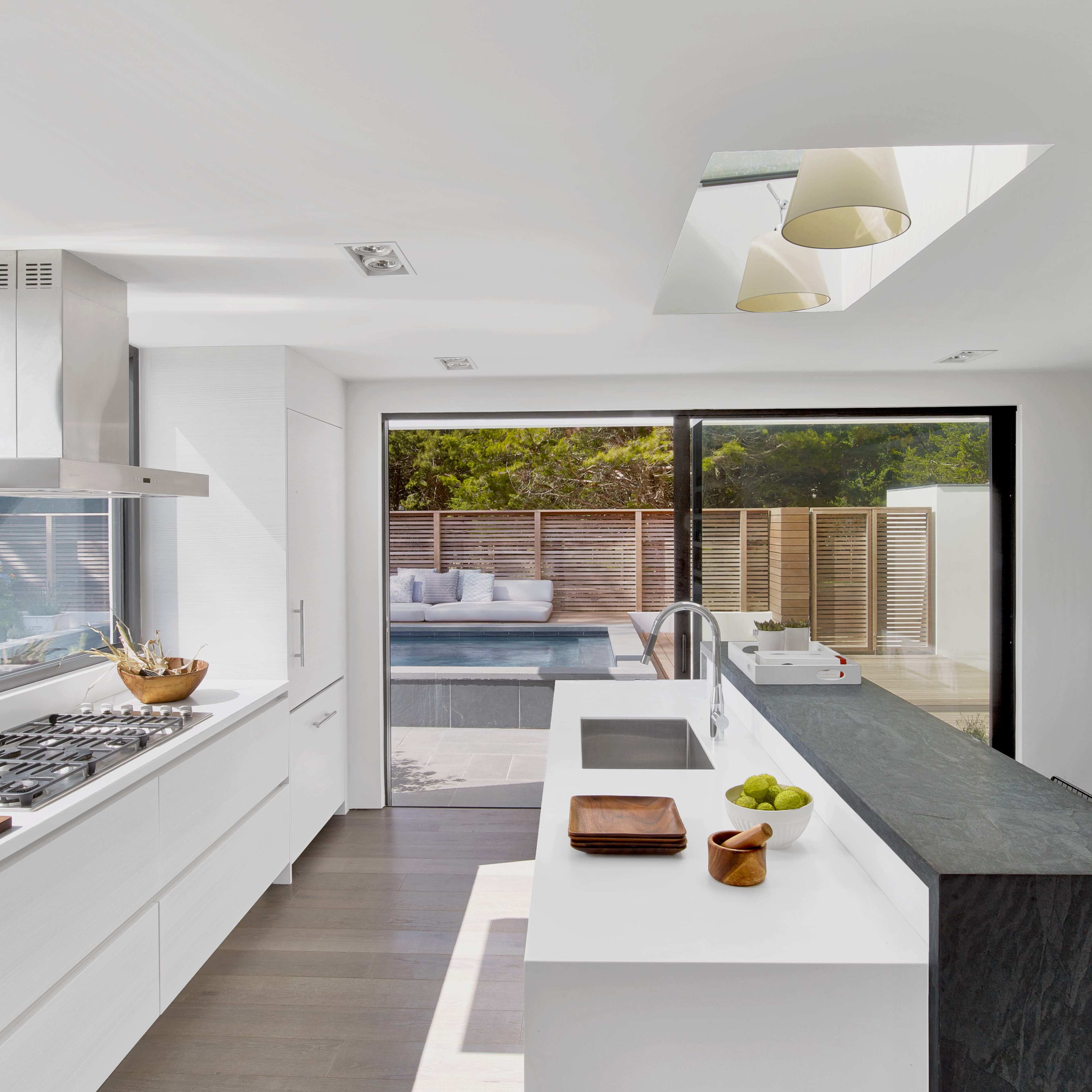 A modern kitchen with white cabinetry, a large window facing a pool area, and a sleek black countertop.