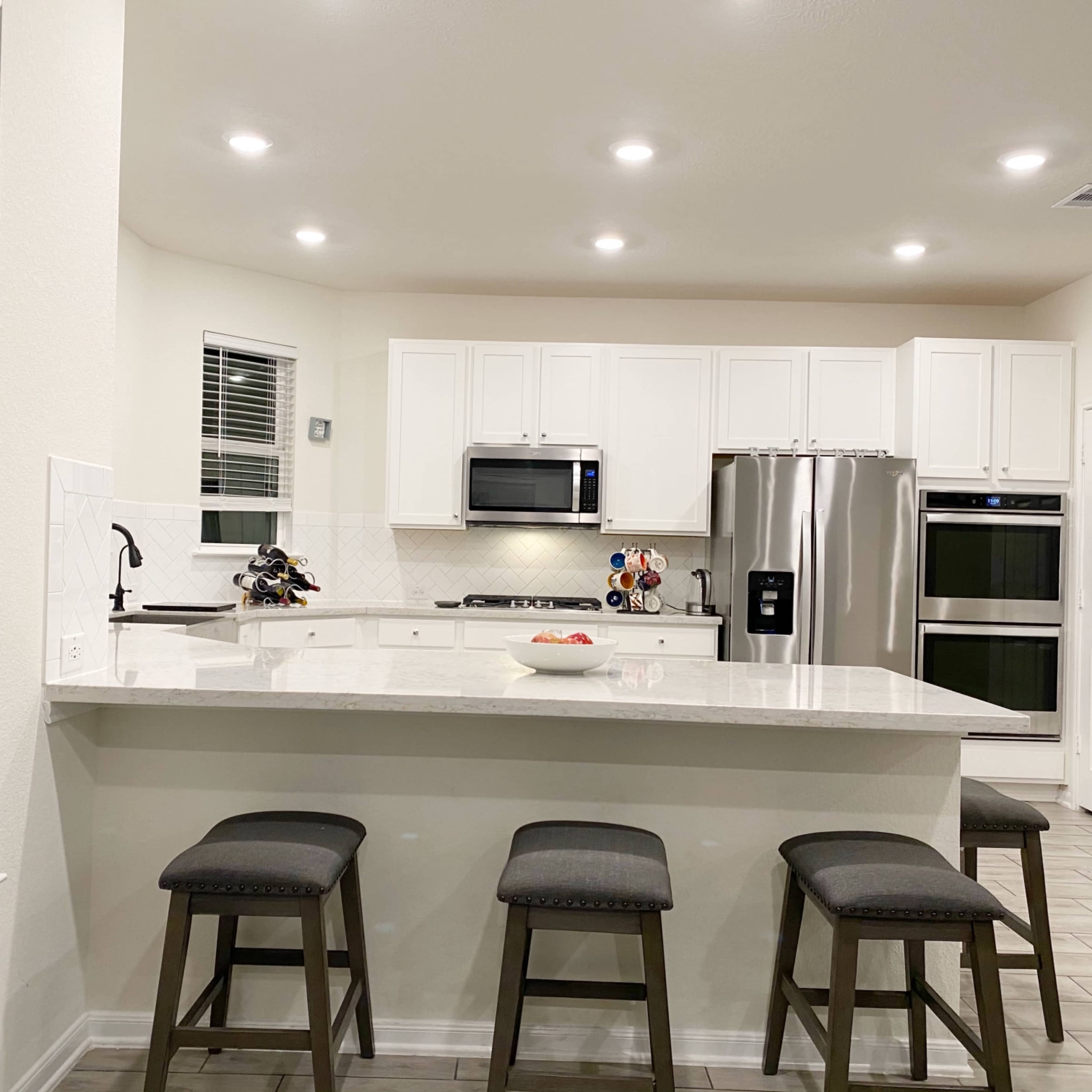 A modern kitchen with white cabinetry, stainless steel appliances, and a central island with four stools.