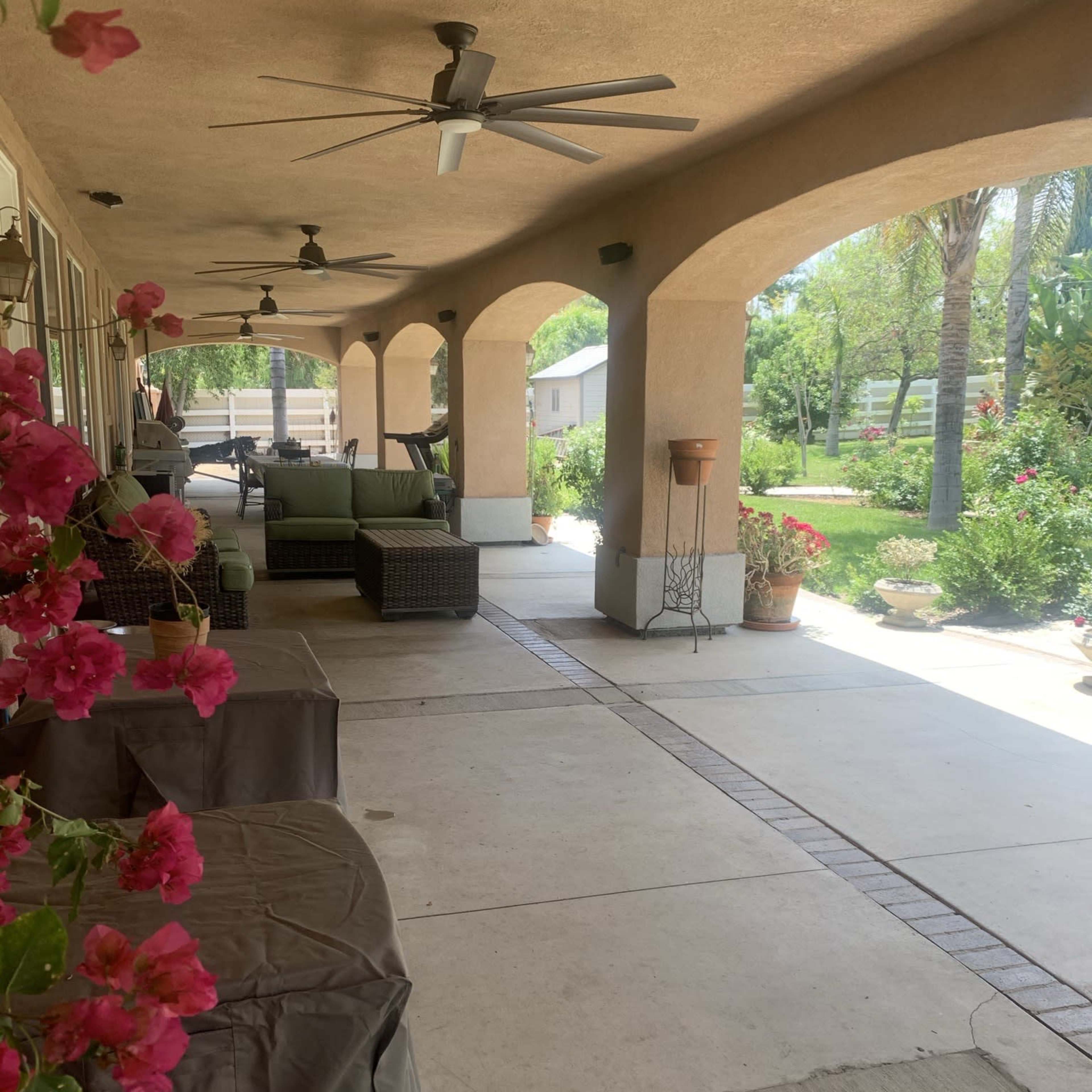A covered patio with wicker furniture and potted plants, bordered by flowering bougainvillea.