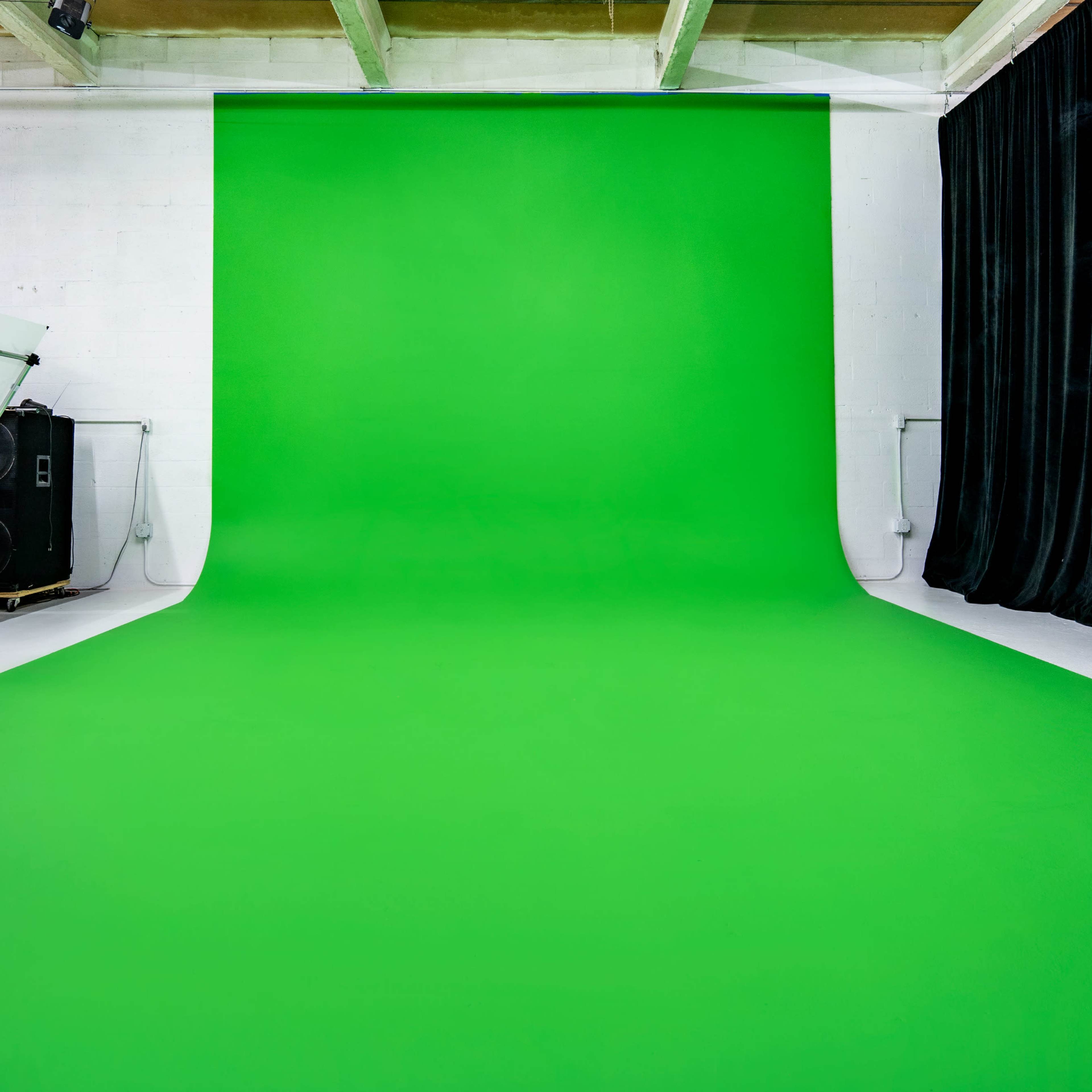 A bright green backdrop is set up in a spacious photo studio, accompanied by equipment on one side.