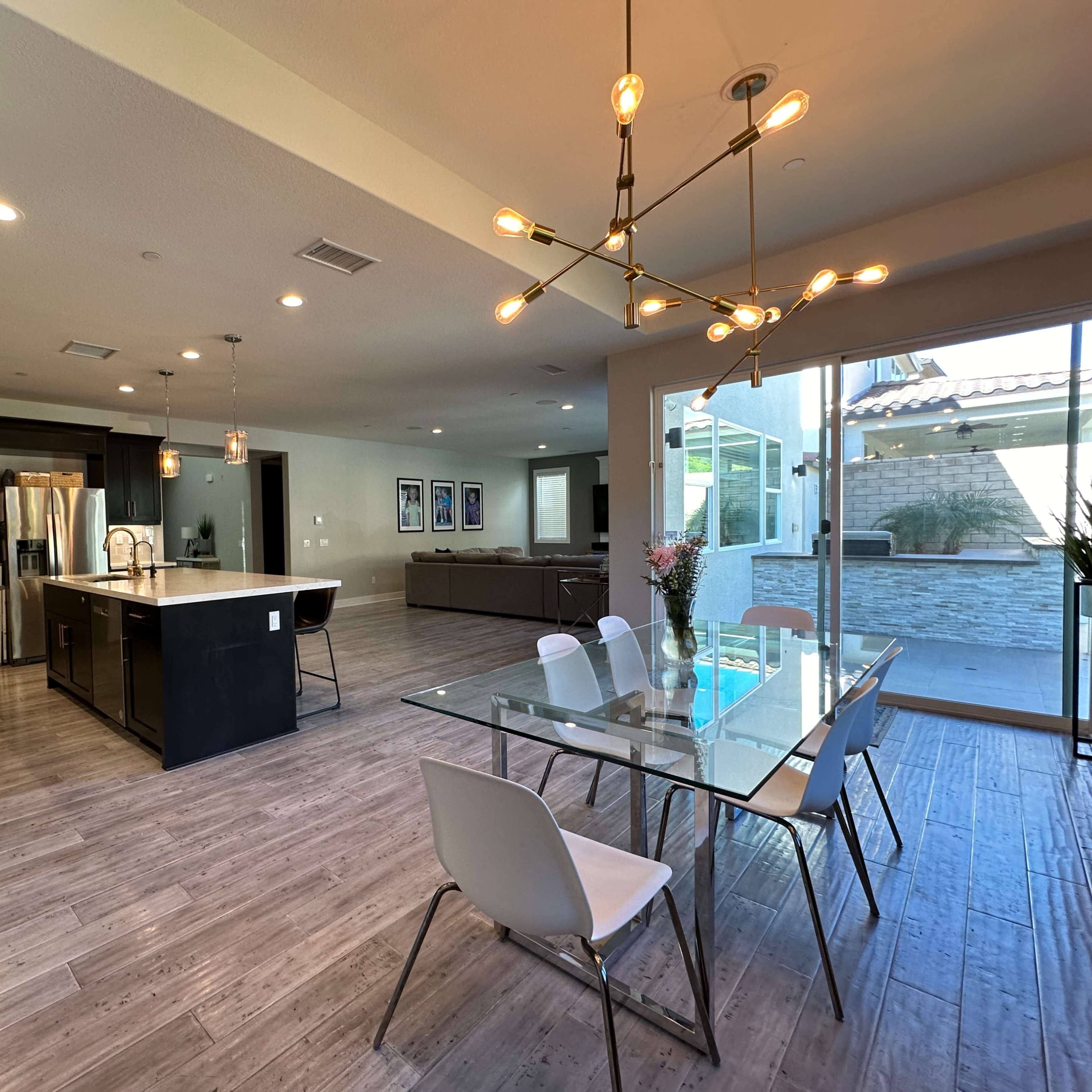 A modern kitchen and dining area featuring an island with a sink, a glass dining table, and large sliding glass doors leading to an outdoor space.