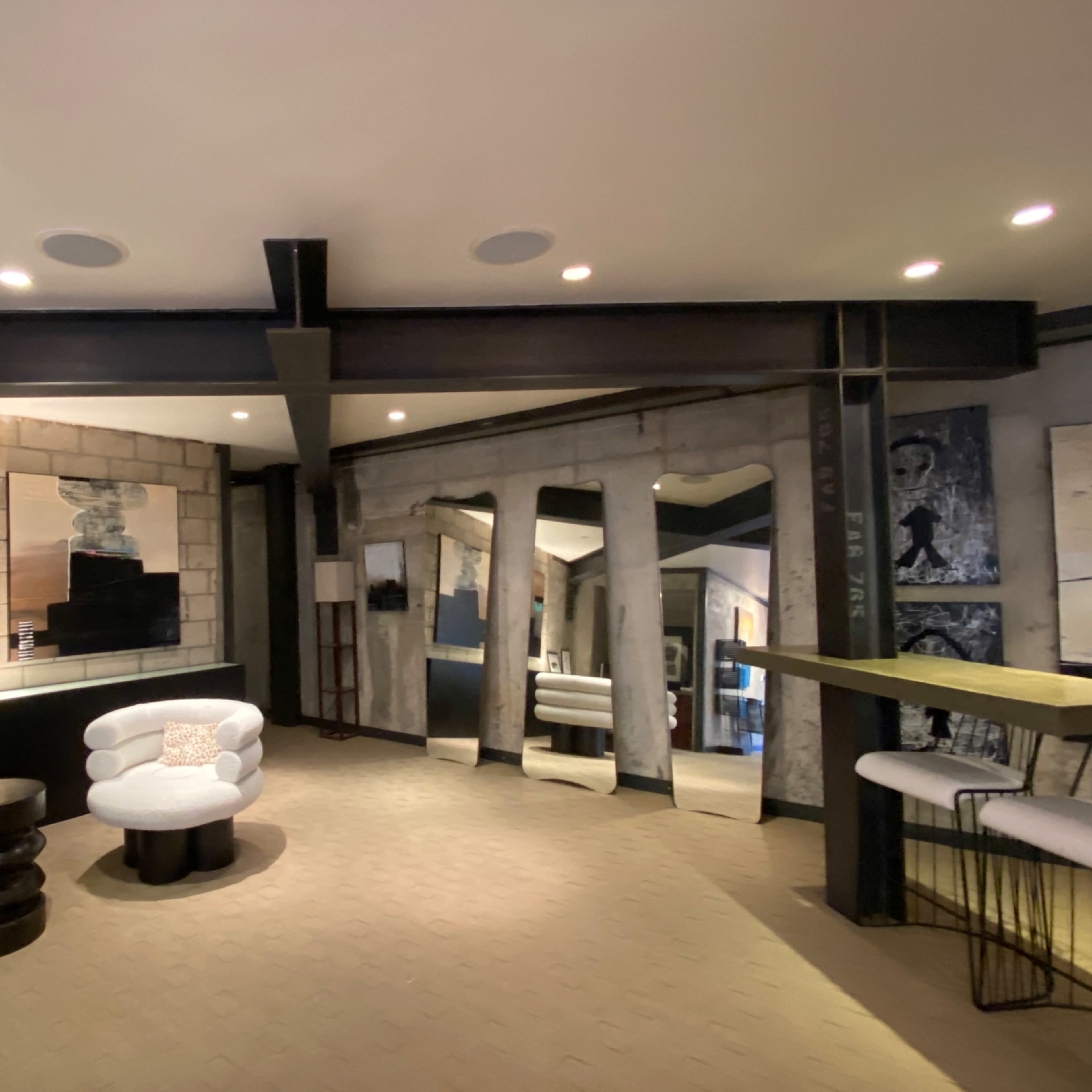 A modern interior space with circular seating arrangements, mixed media artworks on the walls, and a wooden bar counter with a minimalist design.