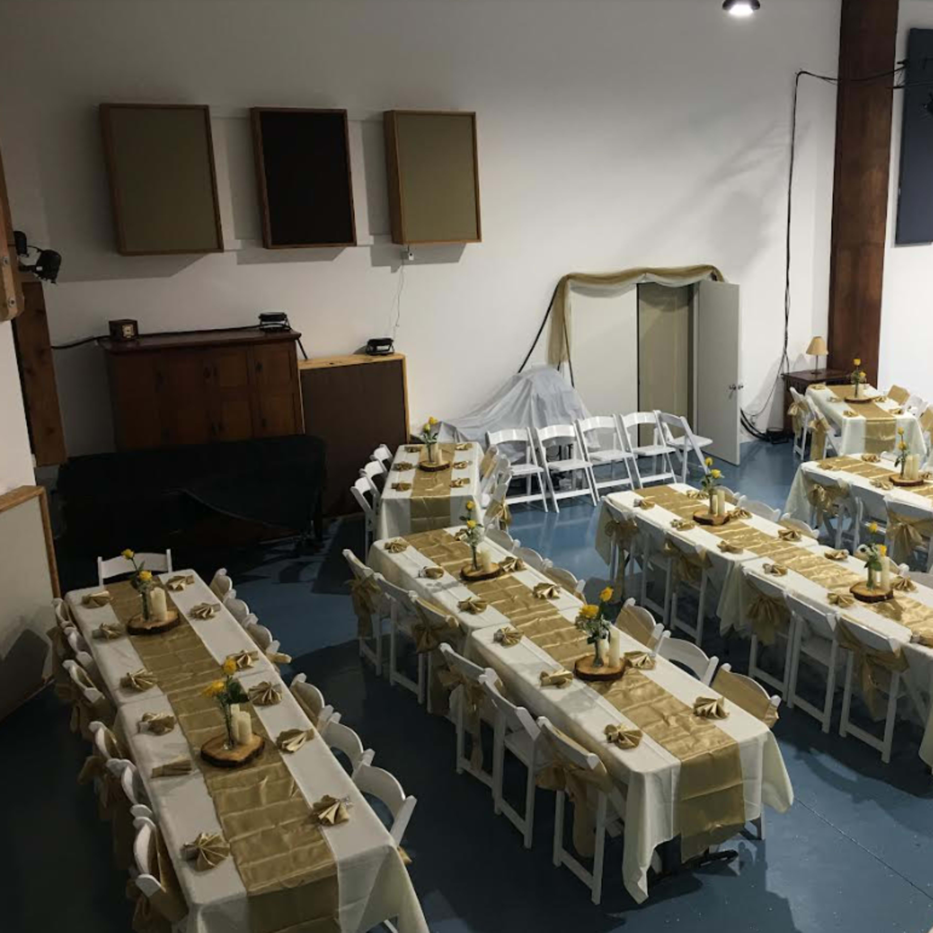 A spacious venue set up with several tables arranged in rows, each covered in cream-colored tablecloths and adorned with yellow floral centerpieces.