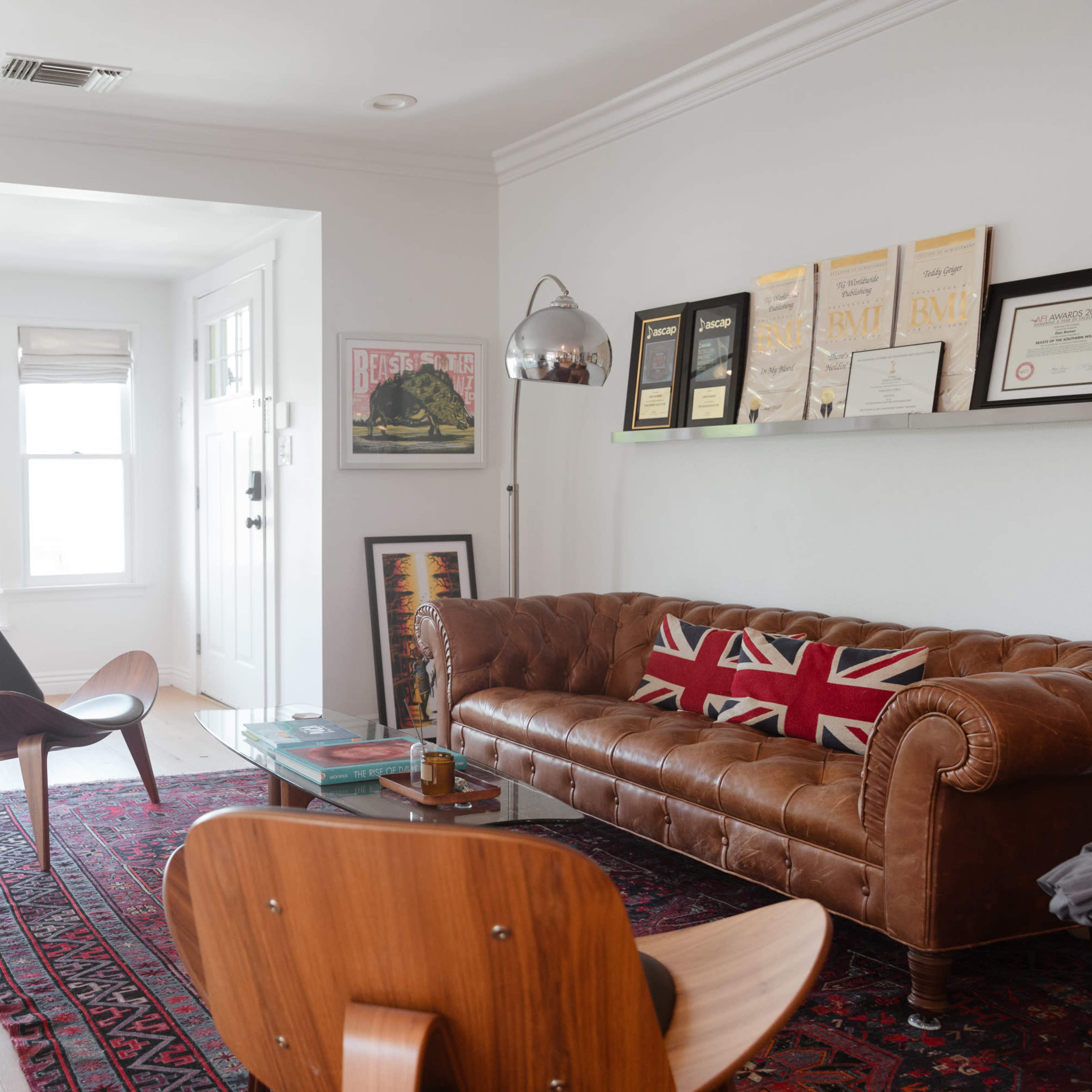 A cozy living room featuring a brown leather Chesterfield sofa adorned with a Union Jack throw, a modern chair, a glass coffee table, and large windows letting in natural light.