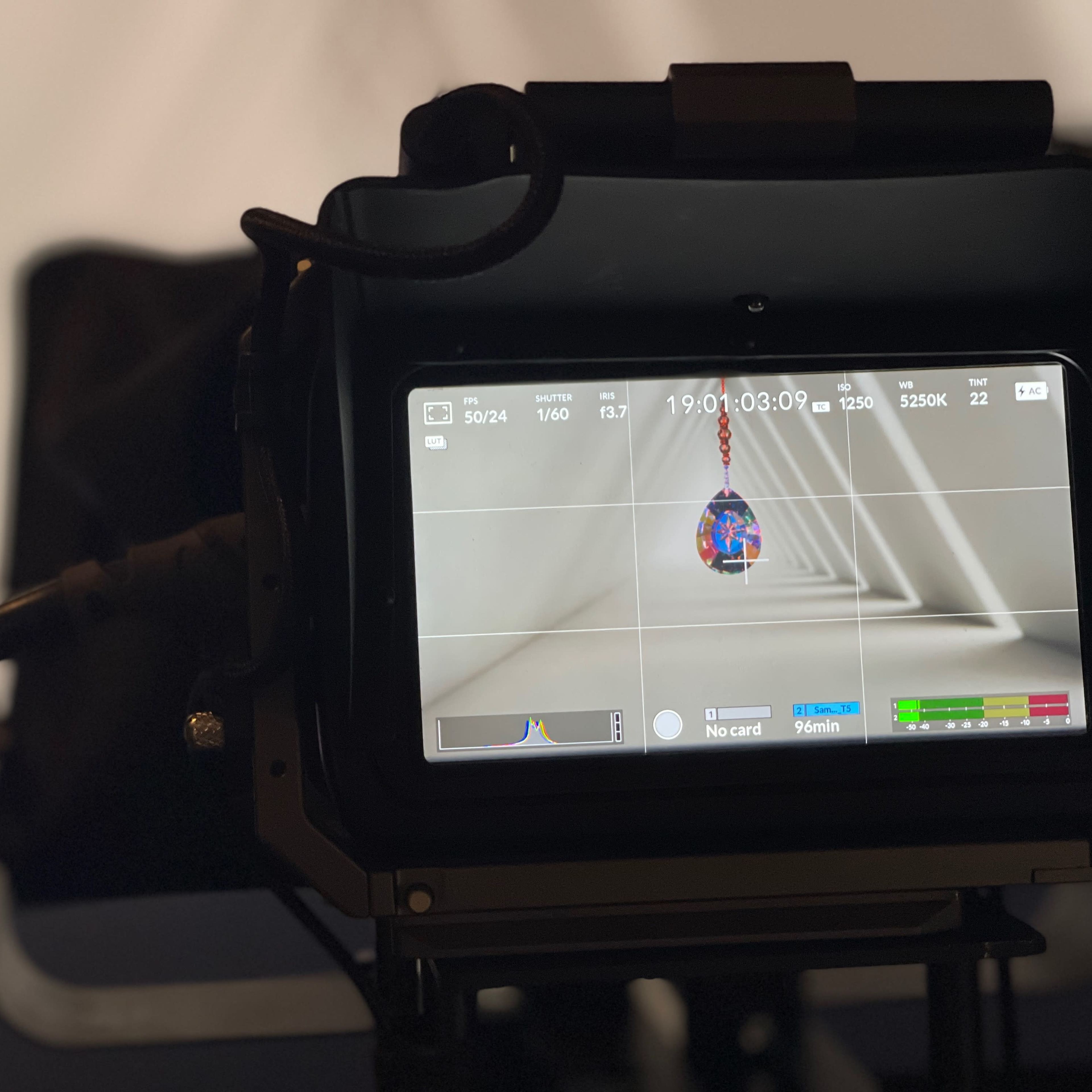 A camera monitor displays a close-up of a colorful object hanging in a structured environment.