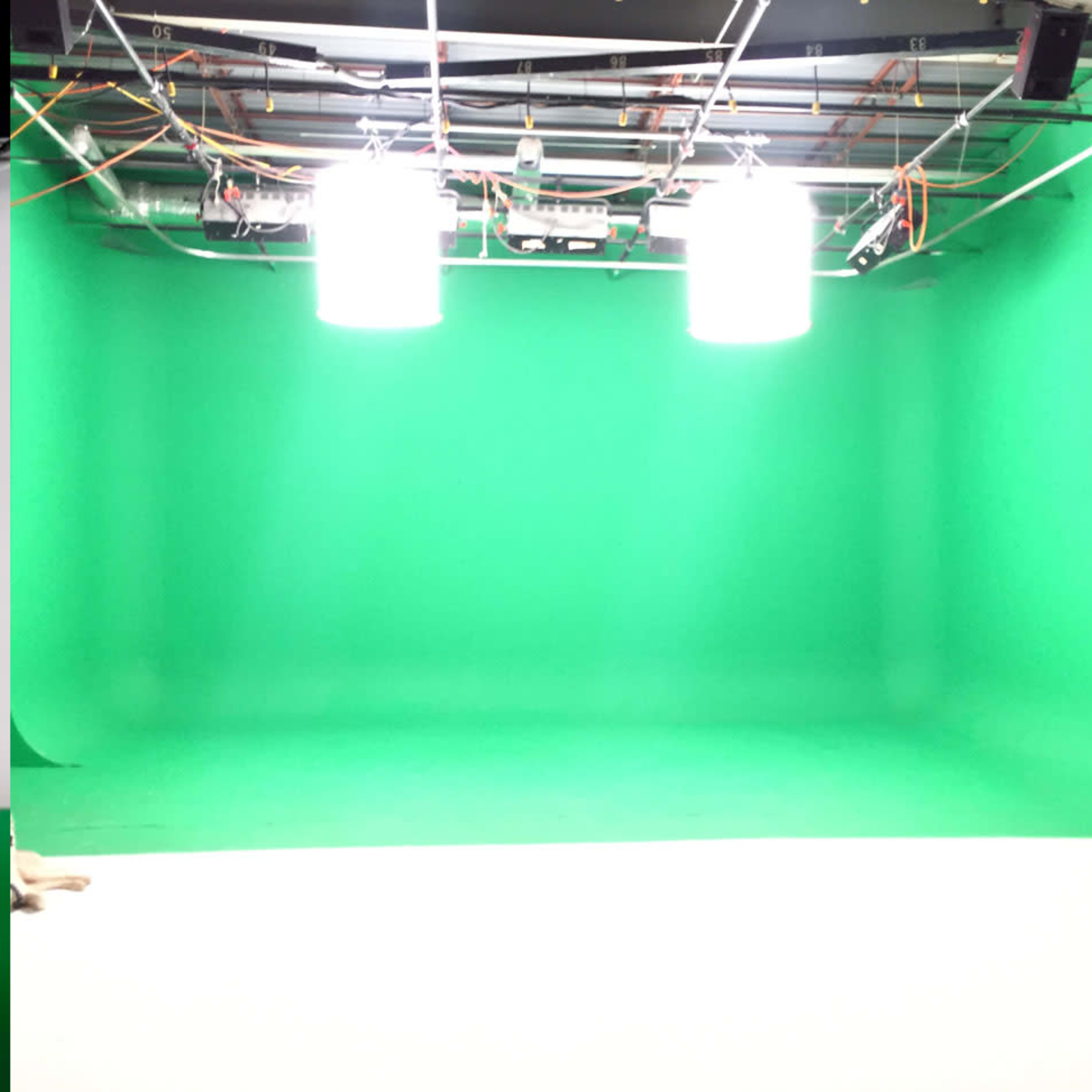 Two studio rooms, one with a white backdrop and the other with a green backdrop, both featuring overhead lights and exposed wiring.