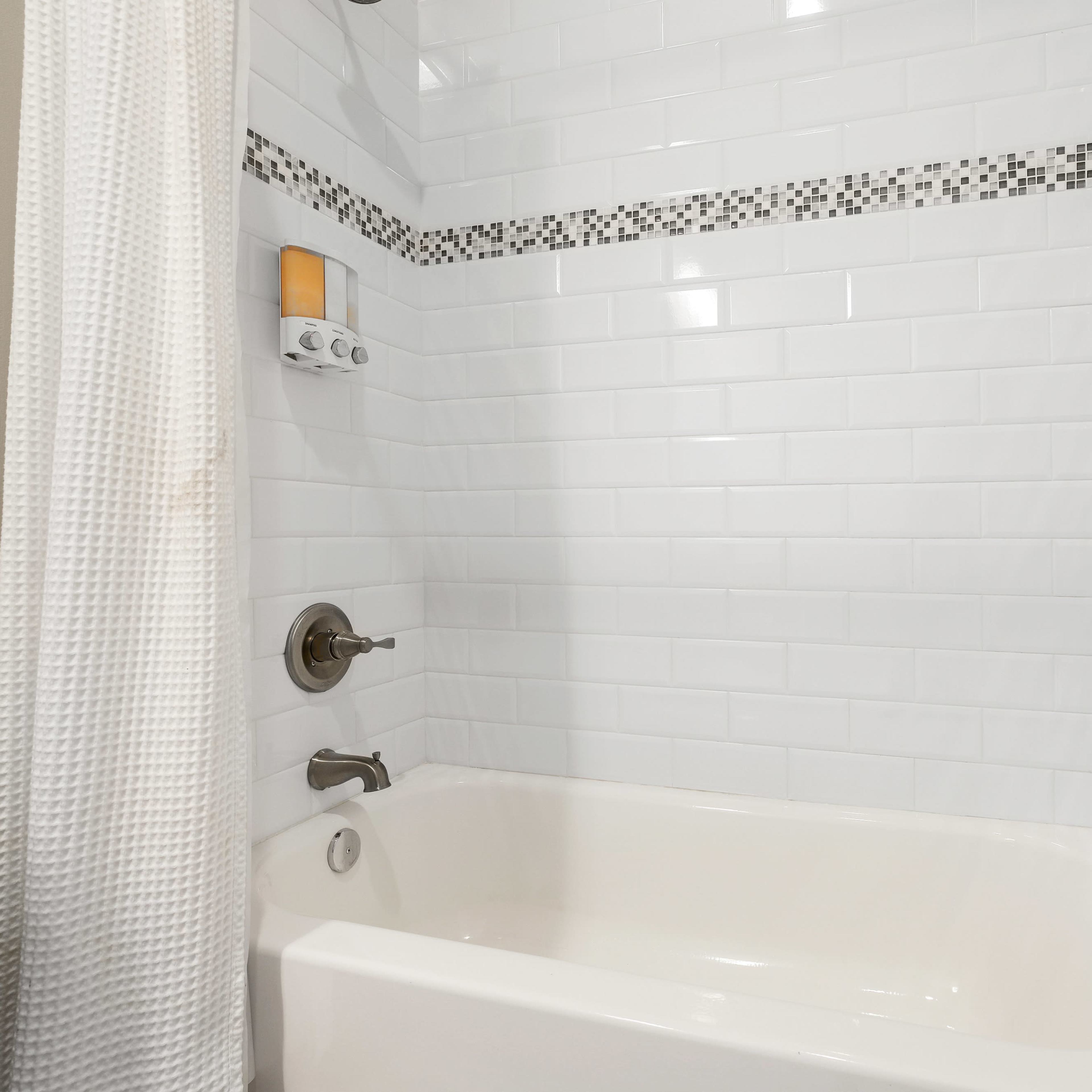 A clean, white tiled shower area with a bathtub and a shower curtain.