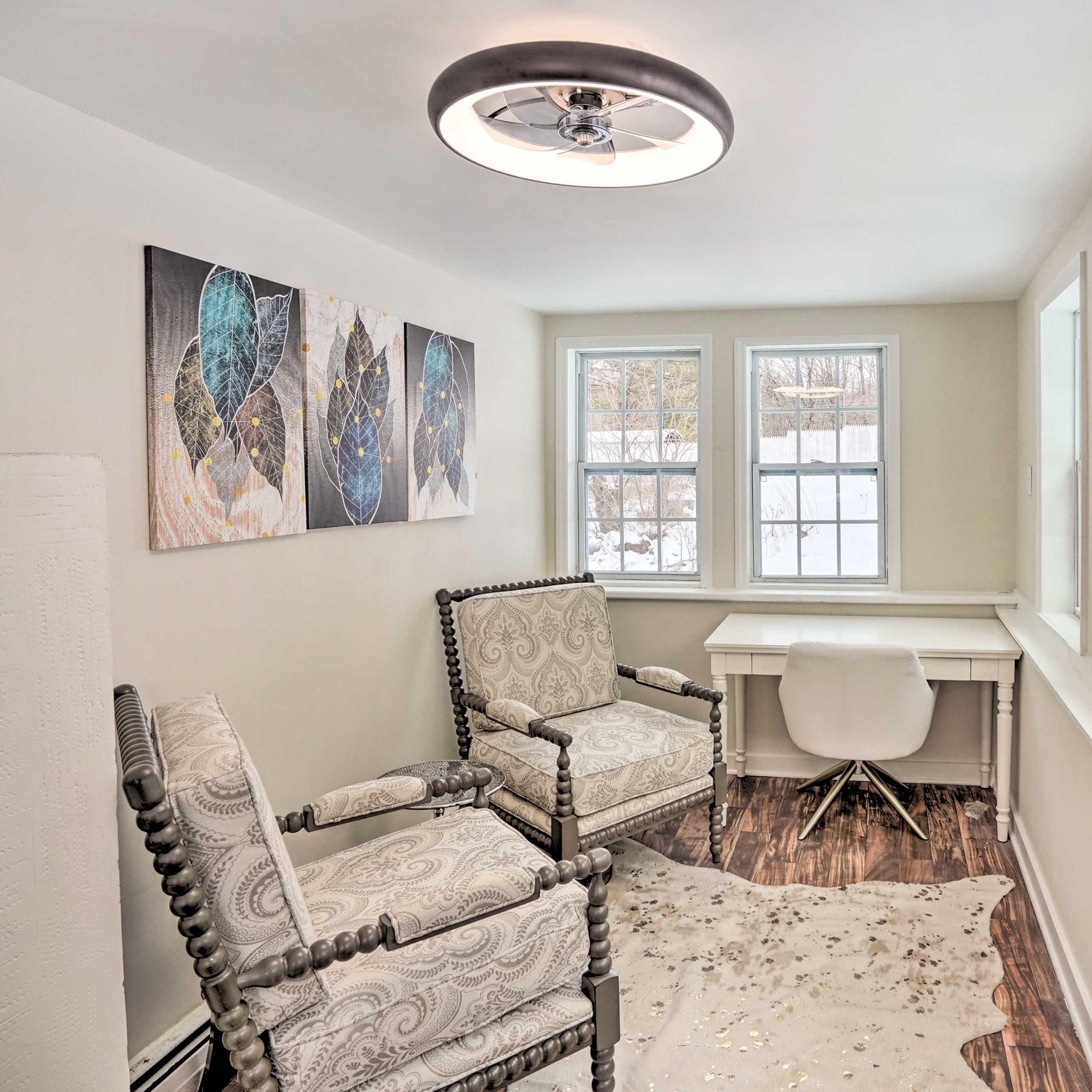A bright, light-colored room features two upholstered chairs, a small white desk, and windows overlooking a snowy landscape.