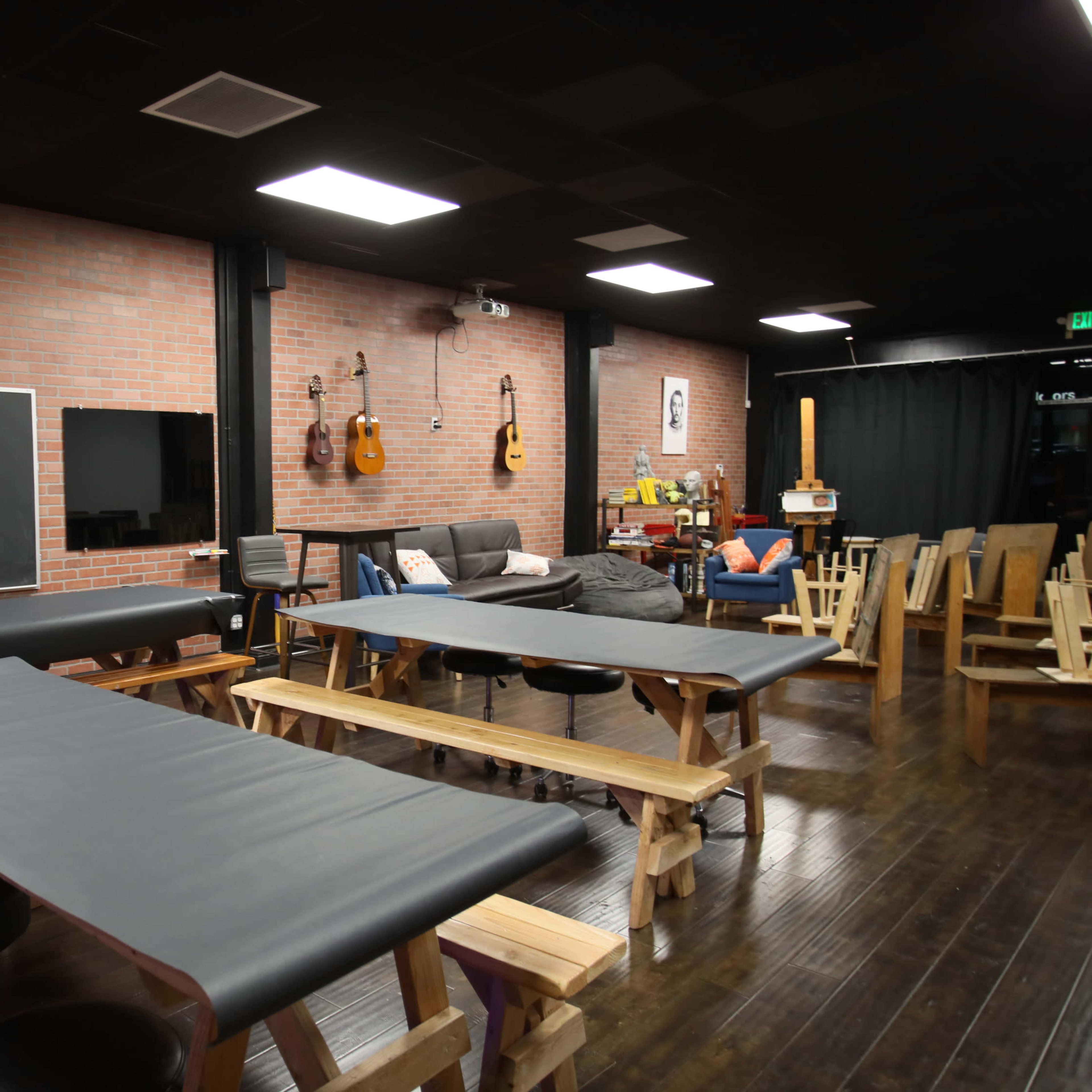 A spacious room with wooden tables and stools, a chalkboard on the wall, and acoustic guitars hanging in the background.