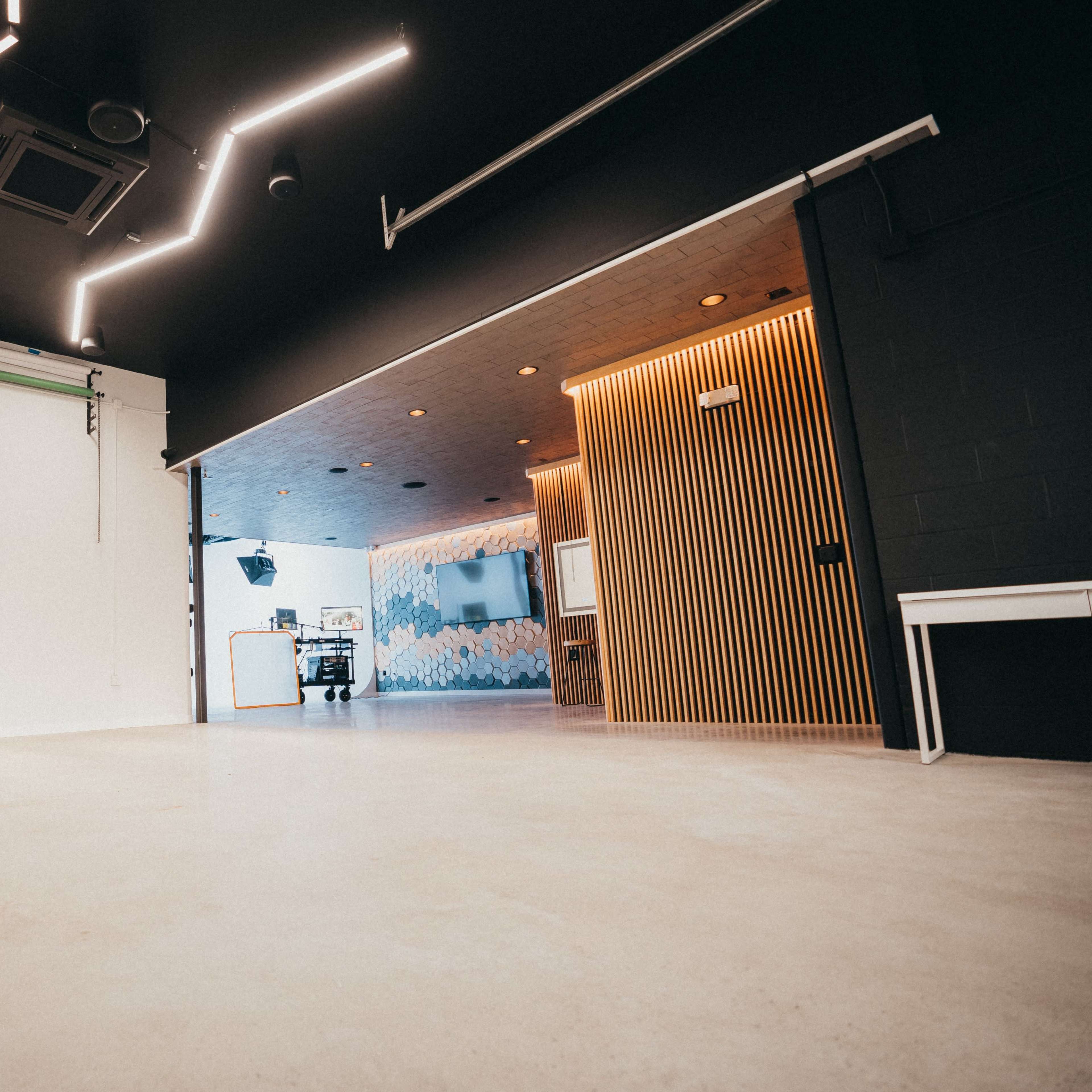 A spacious, modern studio with a lighting setup on wheels, a black wall, and a wooden panel entrance to another area decorated with abstract designs.