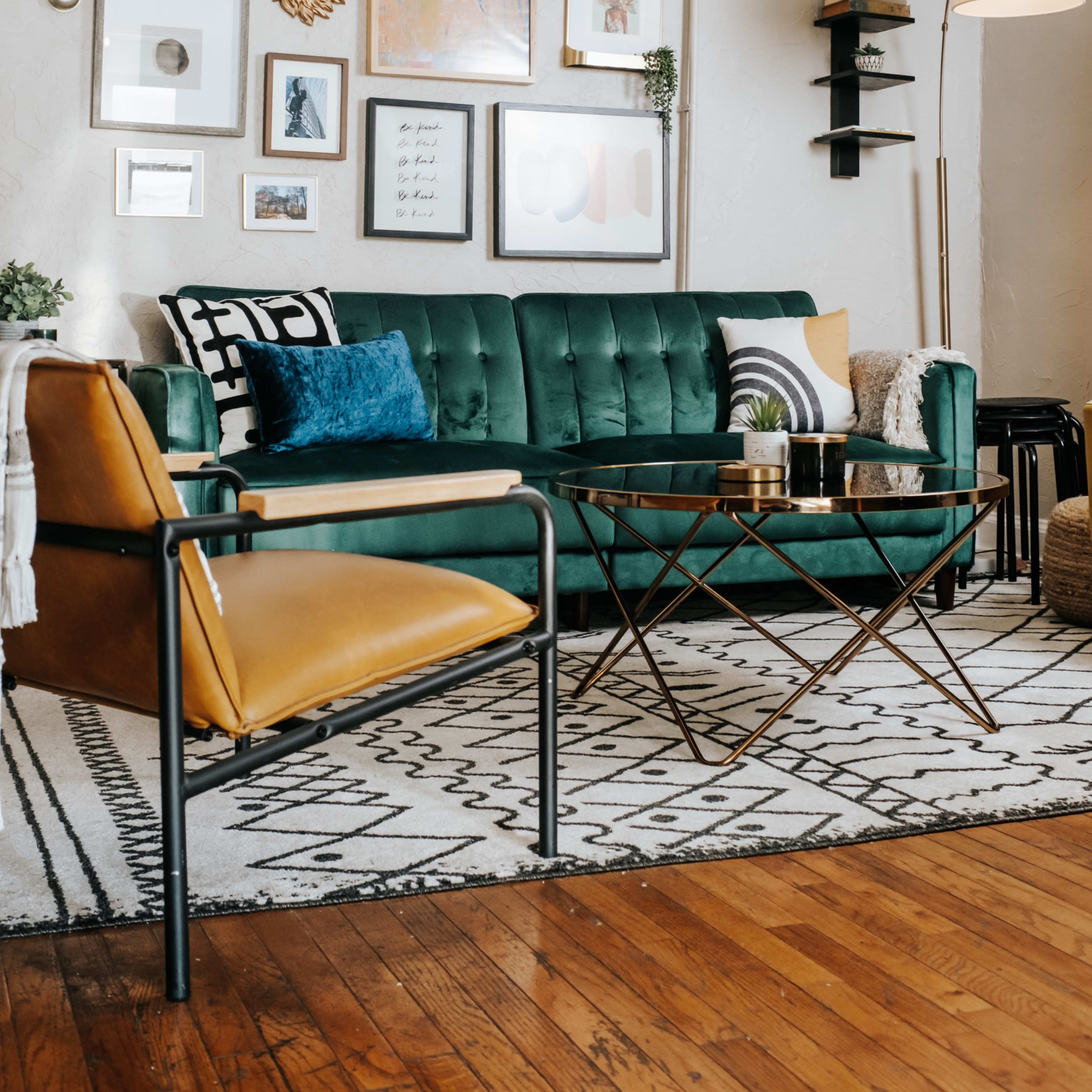 A stylish living room featuring a green velvet sofa, a gallery wall of framed art, and a coffee table set on a patterned rug.
