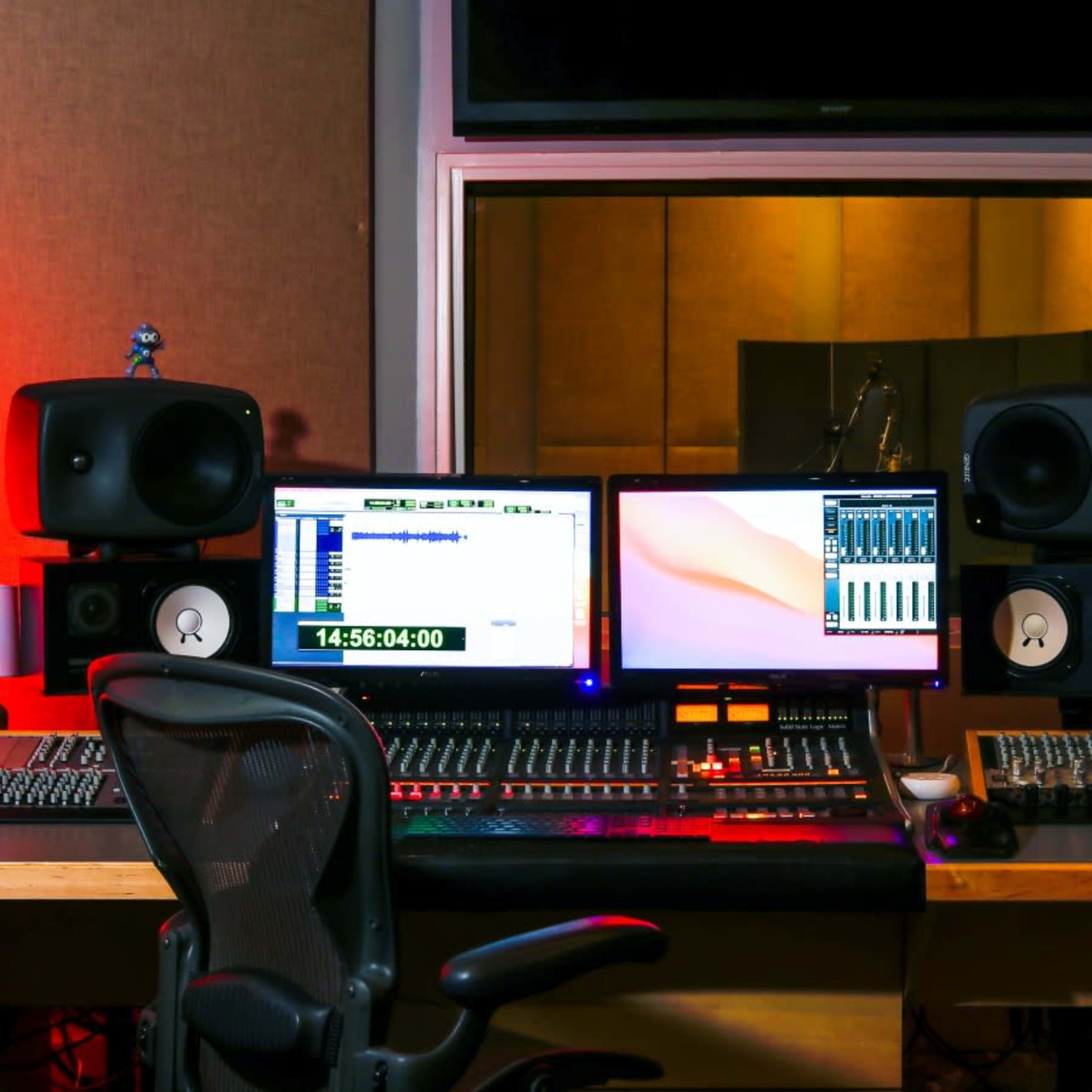 A music production studio featuring a desk with dual computer monitors, audio mixing equipment, and studio speakers.